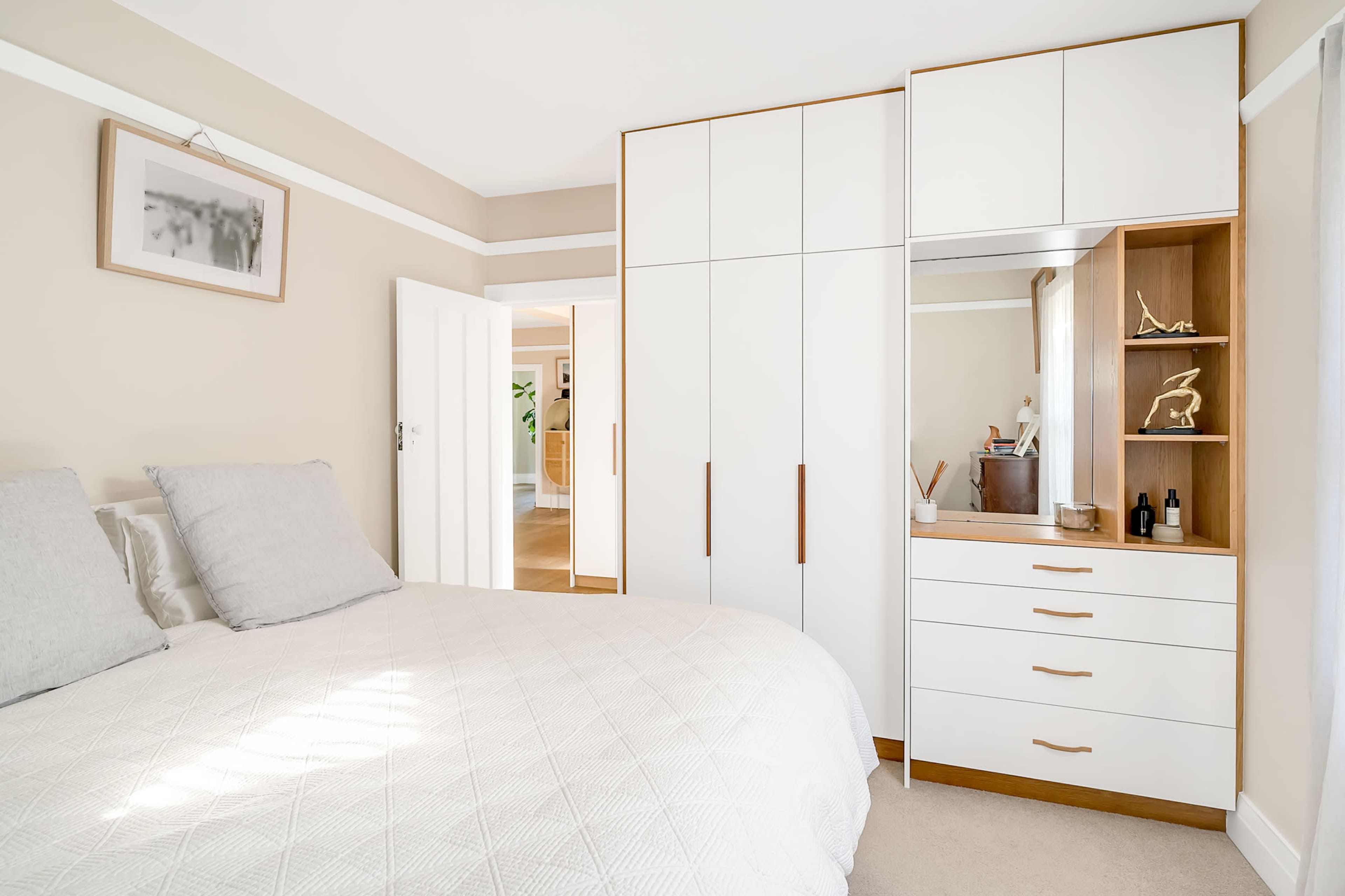 A neatly arranged bedroom features a bed with gray pillows beside a white wardrobe and a dresser with decorative items.