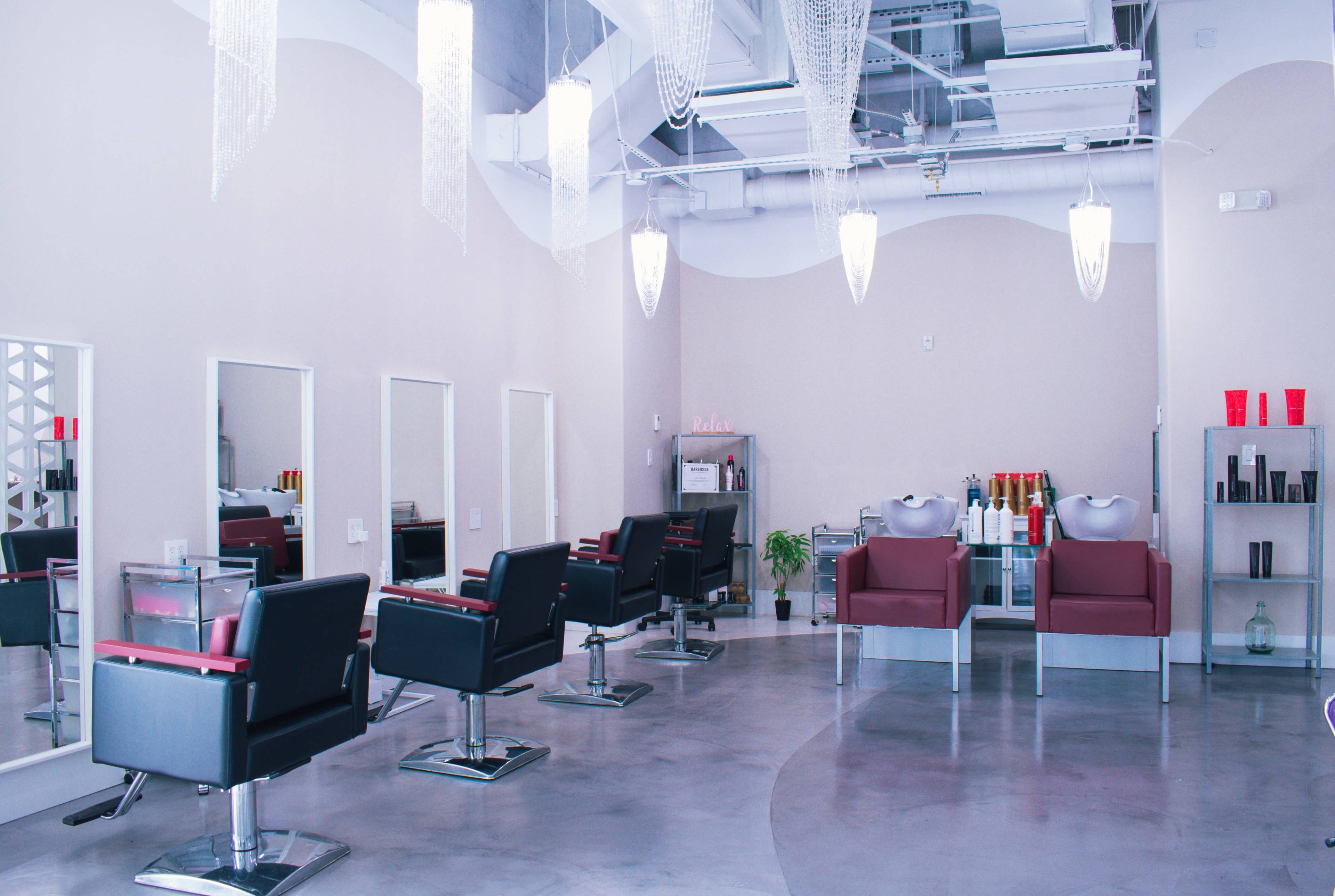 A modern hair salon with several styling chairs, mirrors, and decorative lighting fixtures.