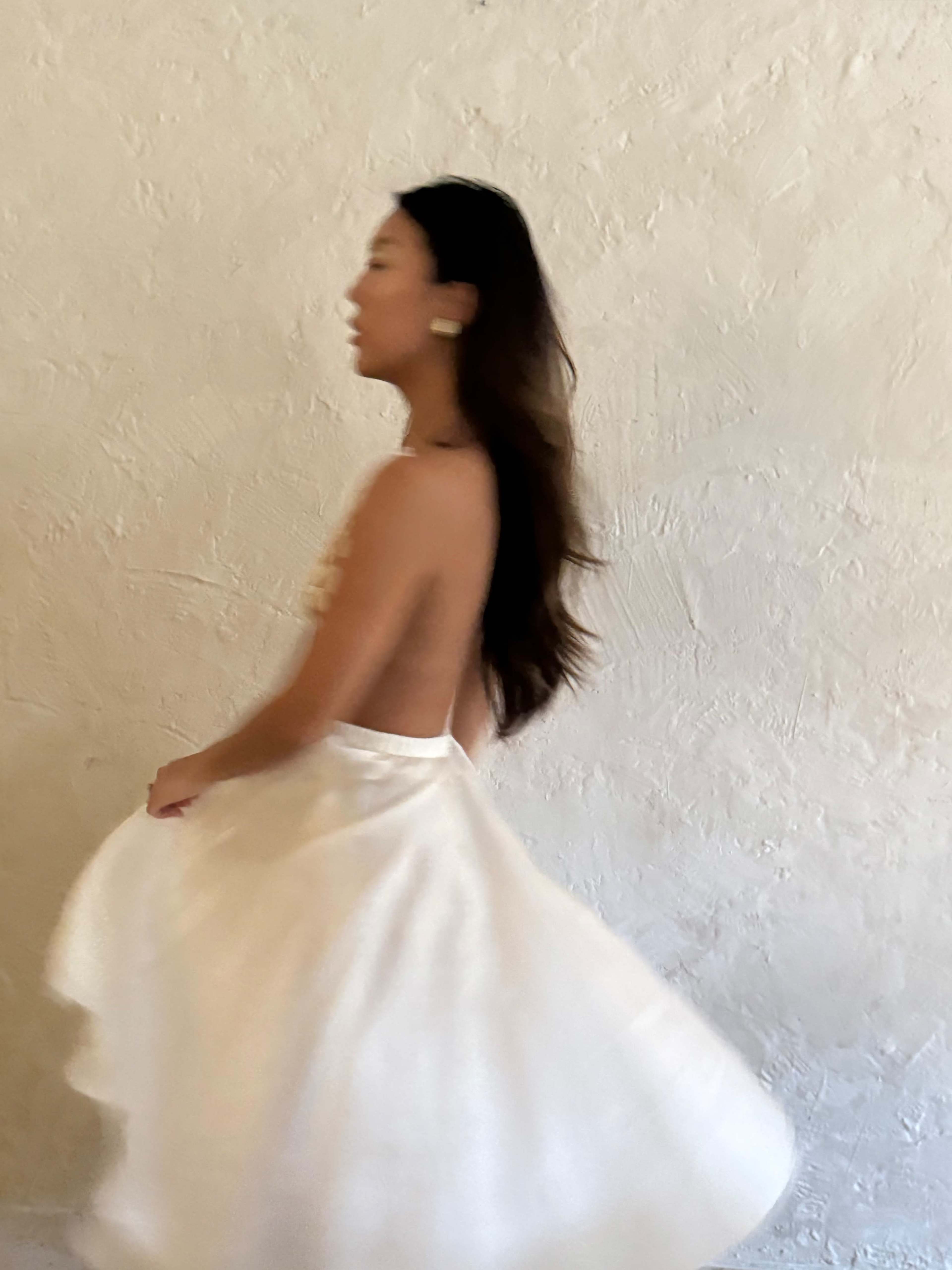A woman in a white dress twirls against a textured wall background.