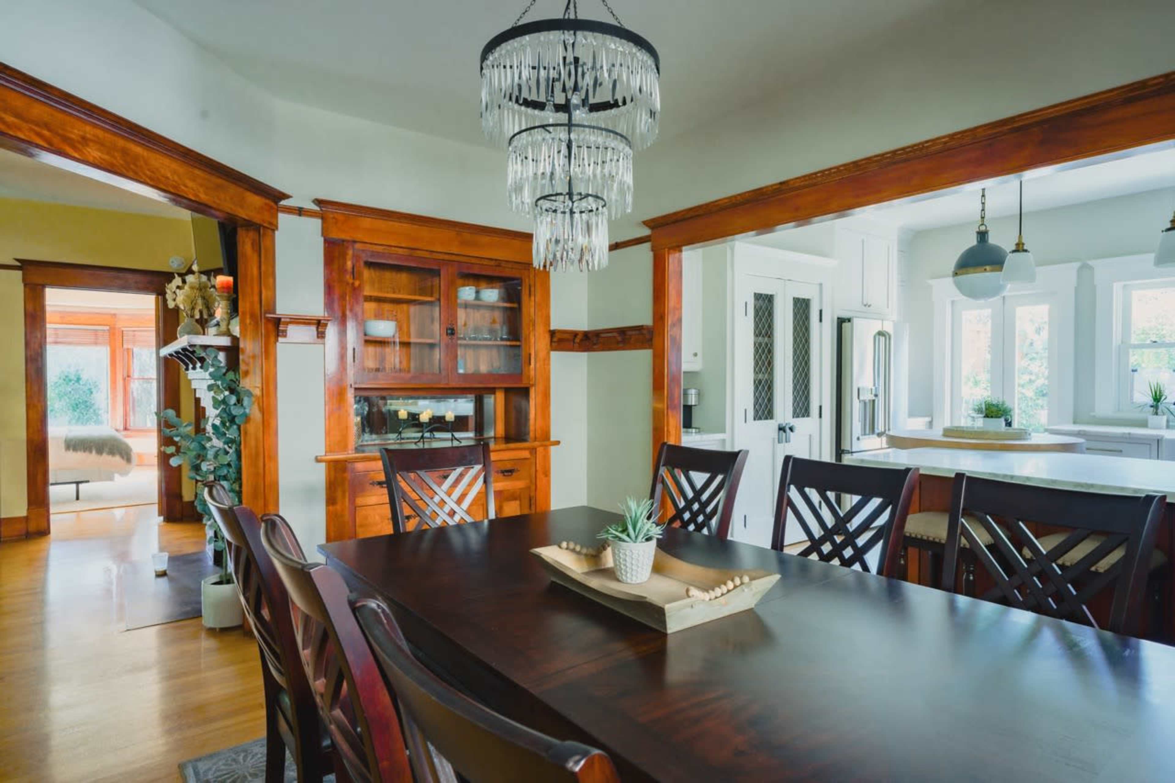 A dining room featuring a wooden table surrounded by chairs, a chandelier overhead, and a built-in cabinet against the wall.