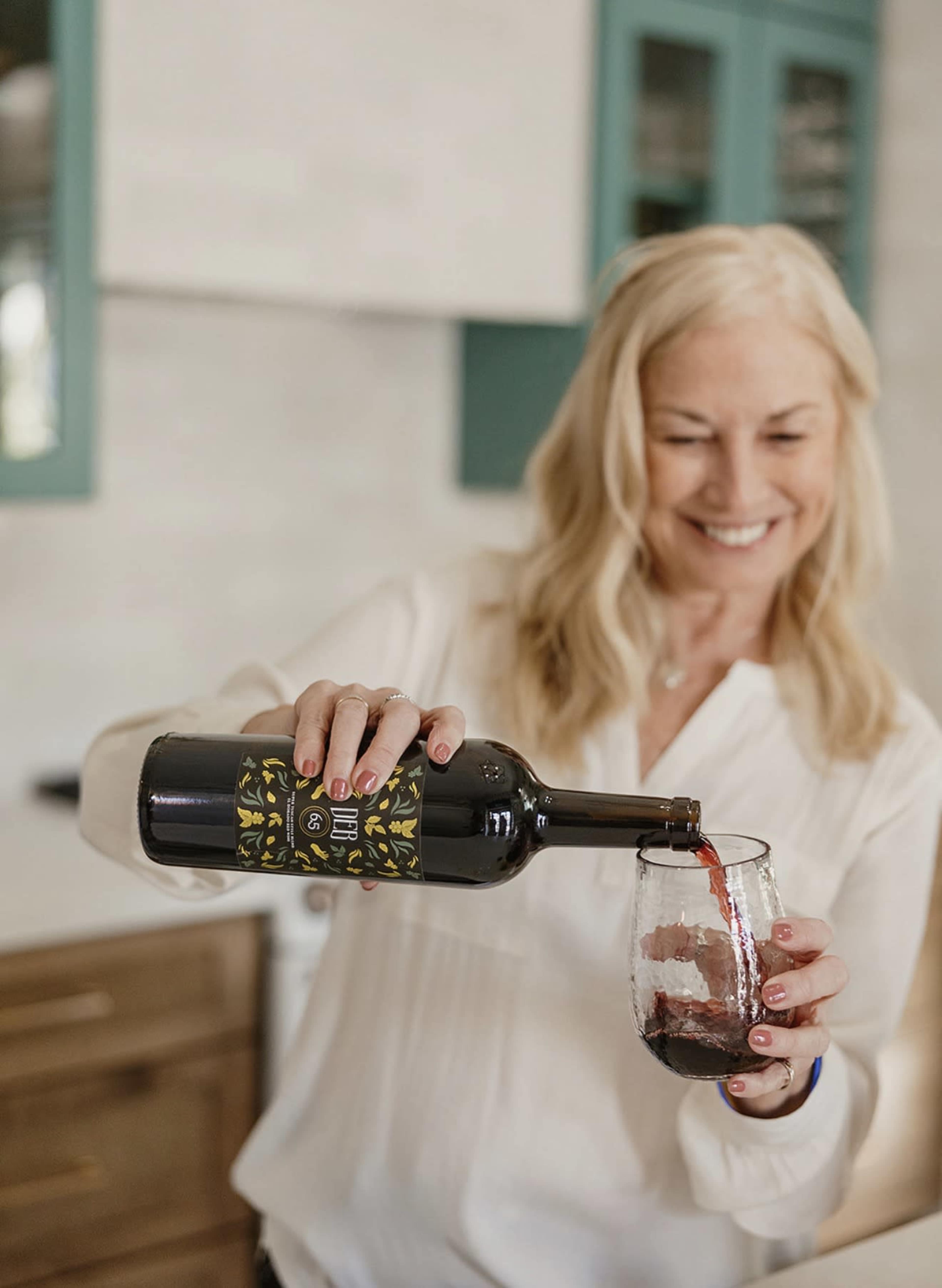 A woman pours red wine from a bottle into a glass in a modern kitchen.