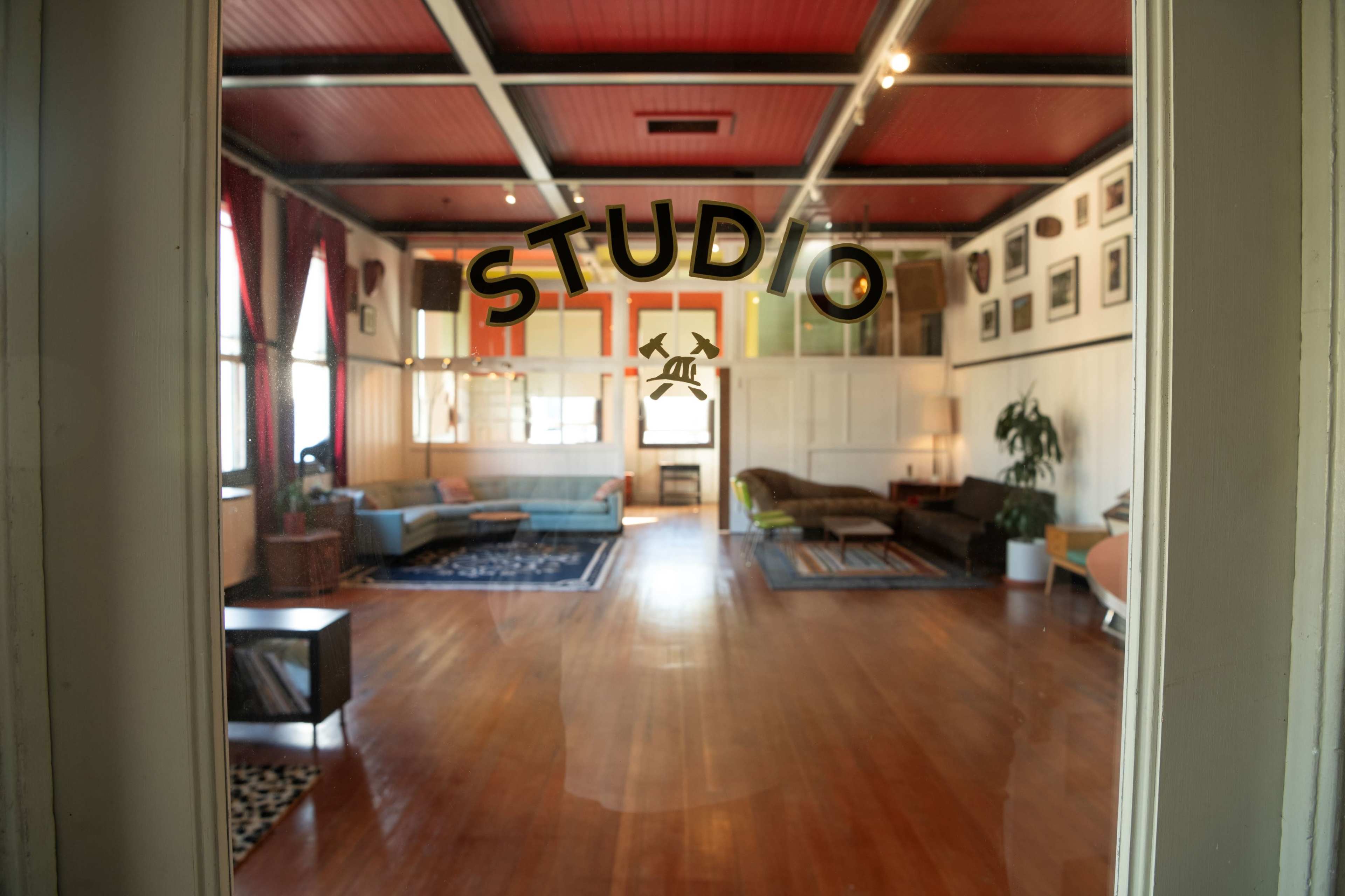A spacious studio with wooden floors, large windows, and a variety of seating arrangements.