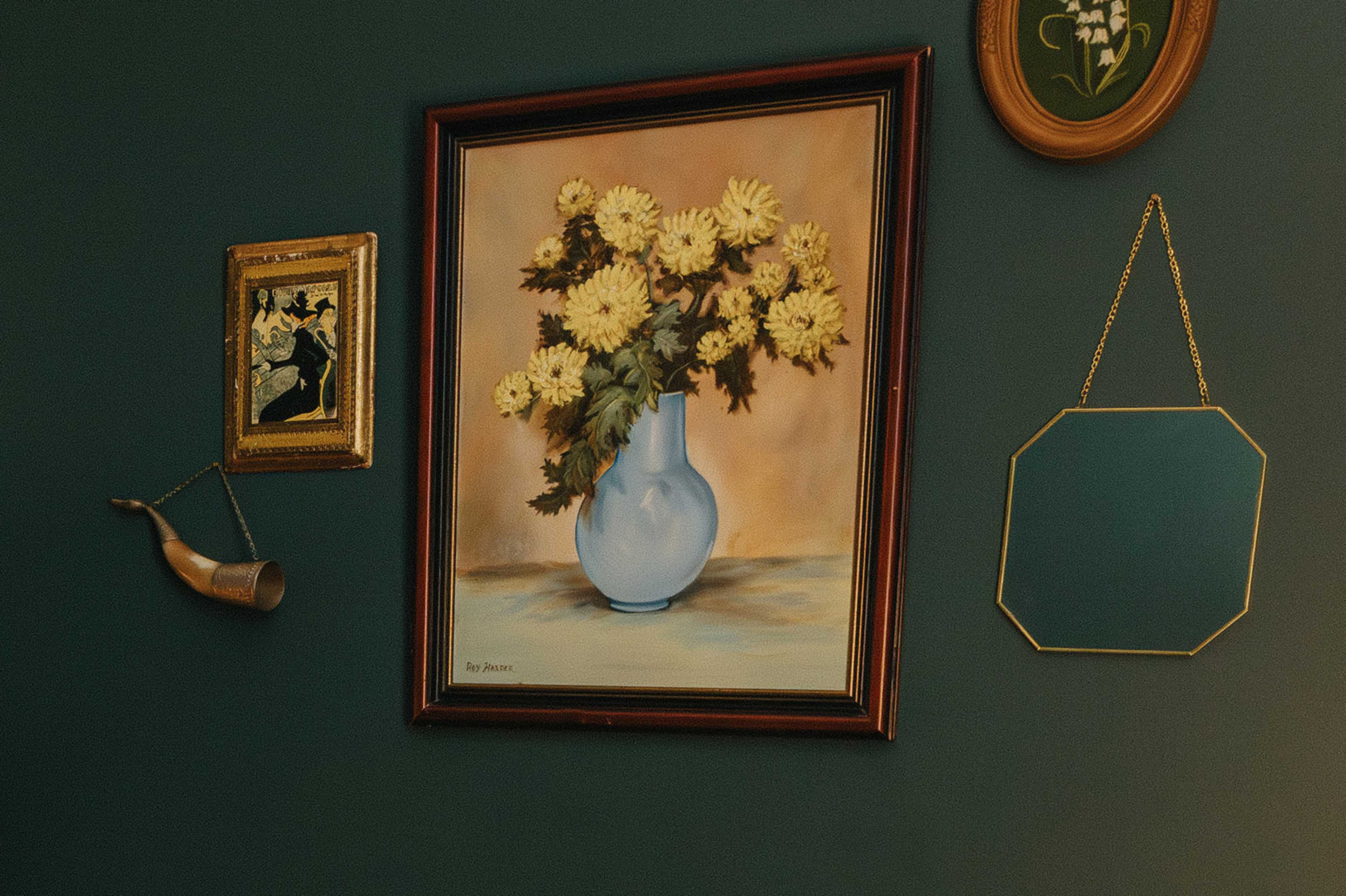 A wall adorned with a floral painting in a frame, a small framed artwork, an ornate mirror, and a decorative horn.