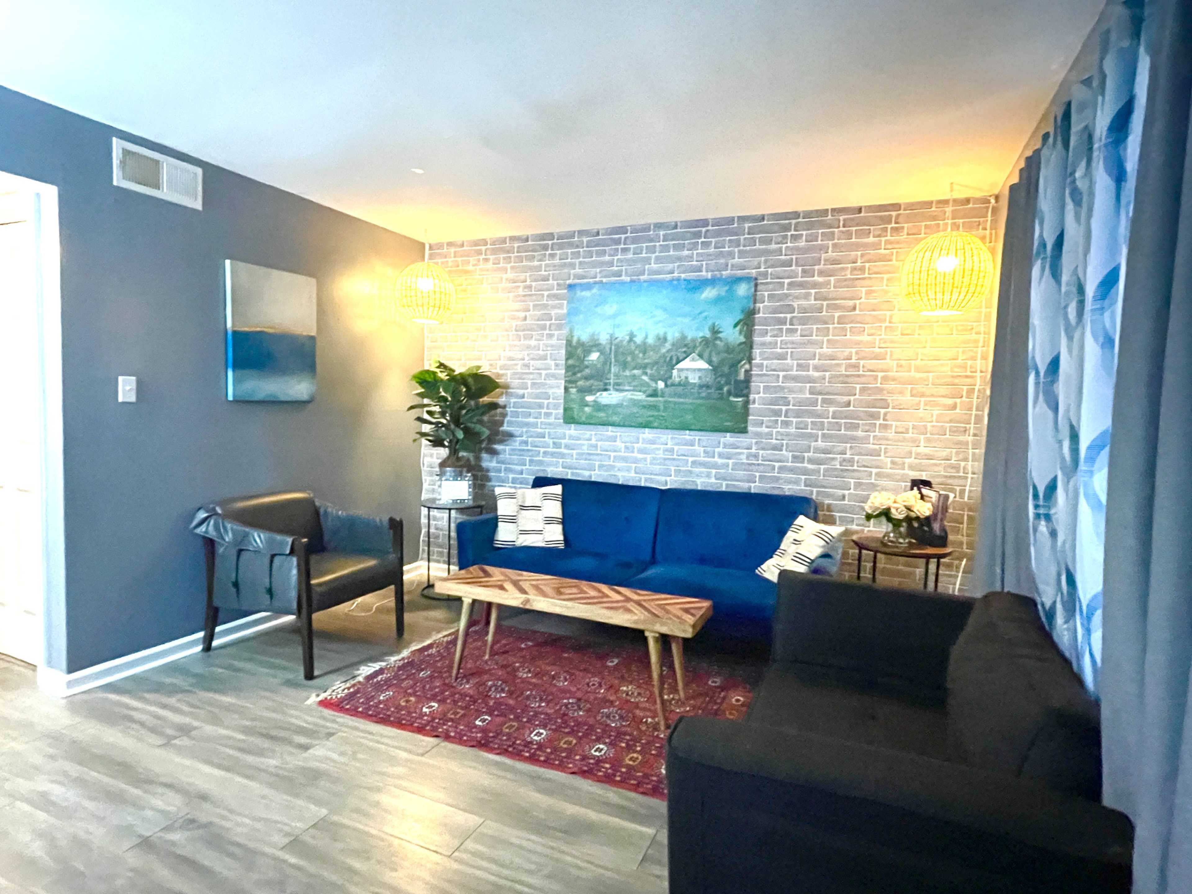 The image shows a modern living room featuring a blue sofa, a wooden coffee table on a red area rug, and two decorative pendant lights illuminating the space.