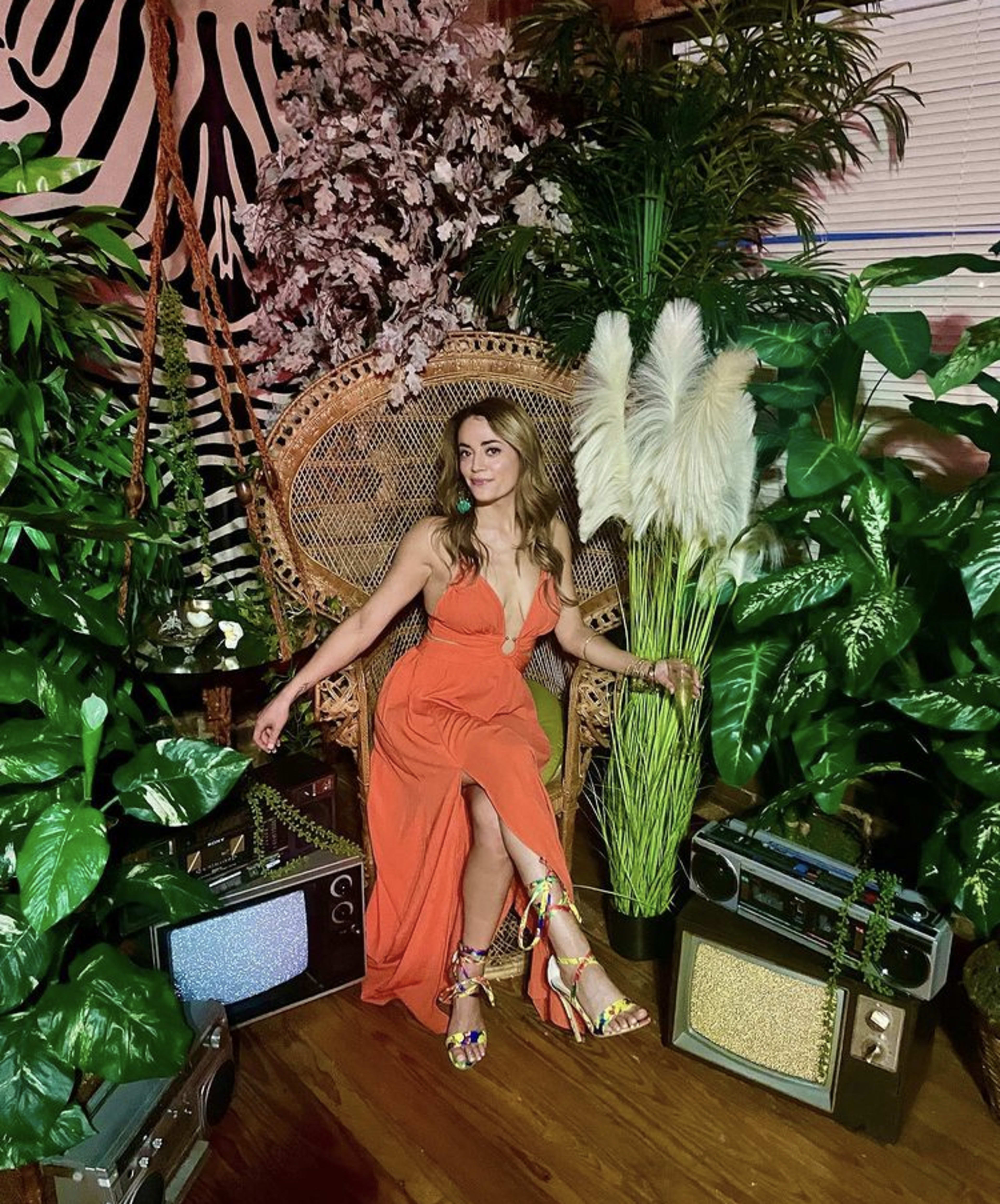 A woman in a red dress sitting in a chair surrounded by plants.