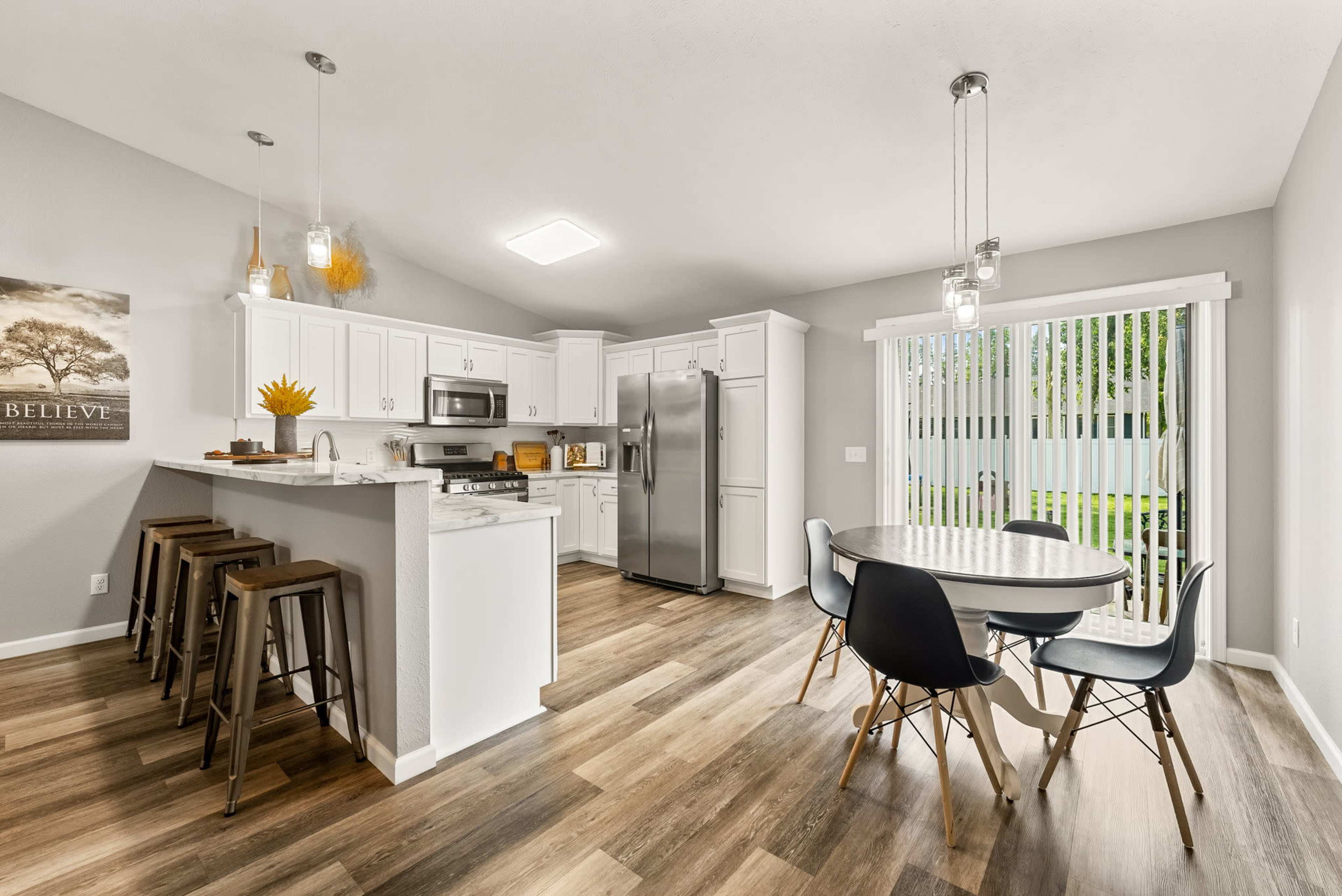 A modern kitchen and dining area with white cabinetry, a gray color scheme, a round dining table, and bar stools at a breakfast bar.