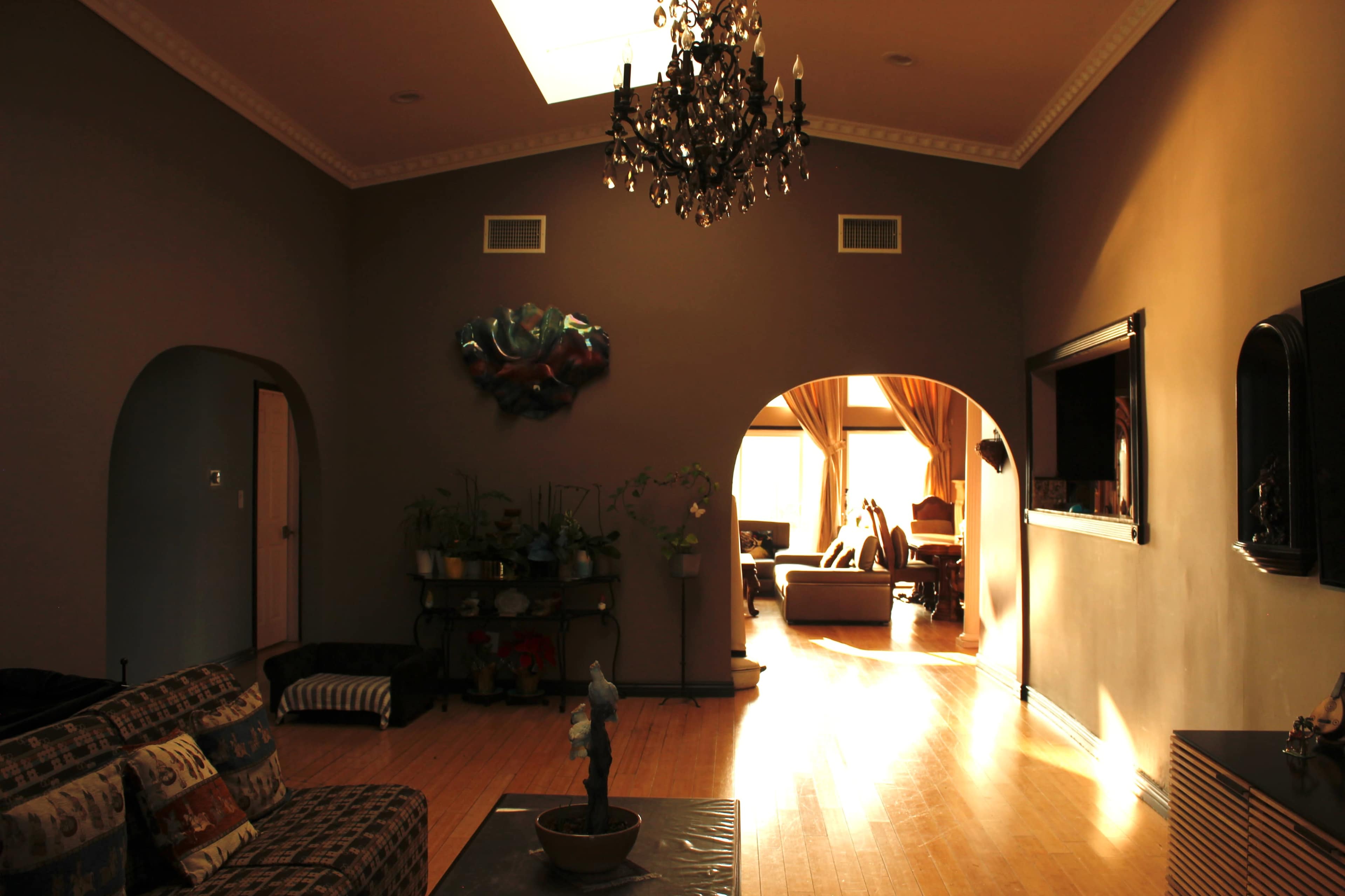 A spacious living room with hardwood floors, a chandelier, and large windows illuminating the area.