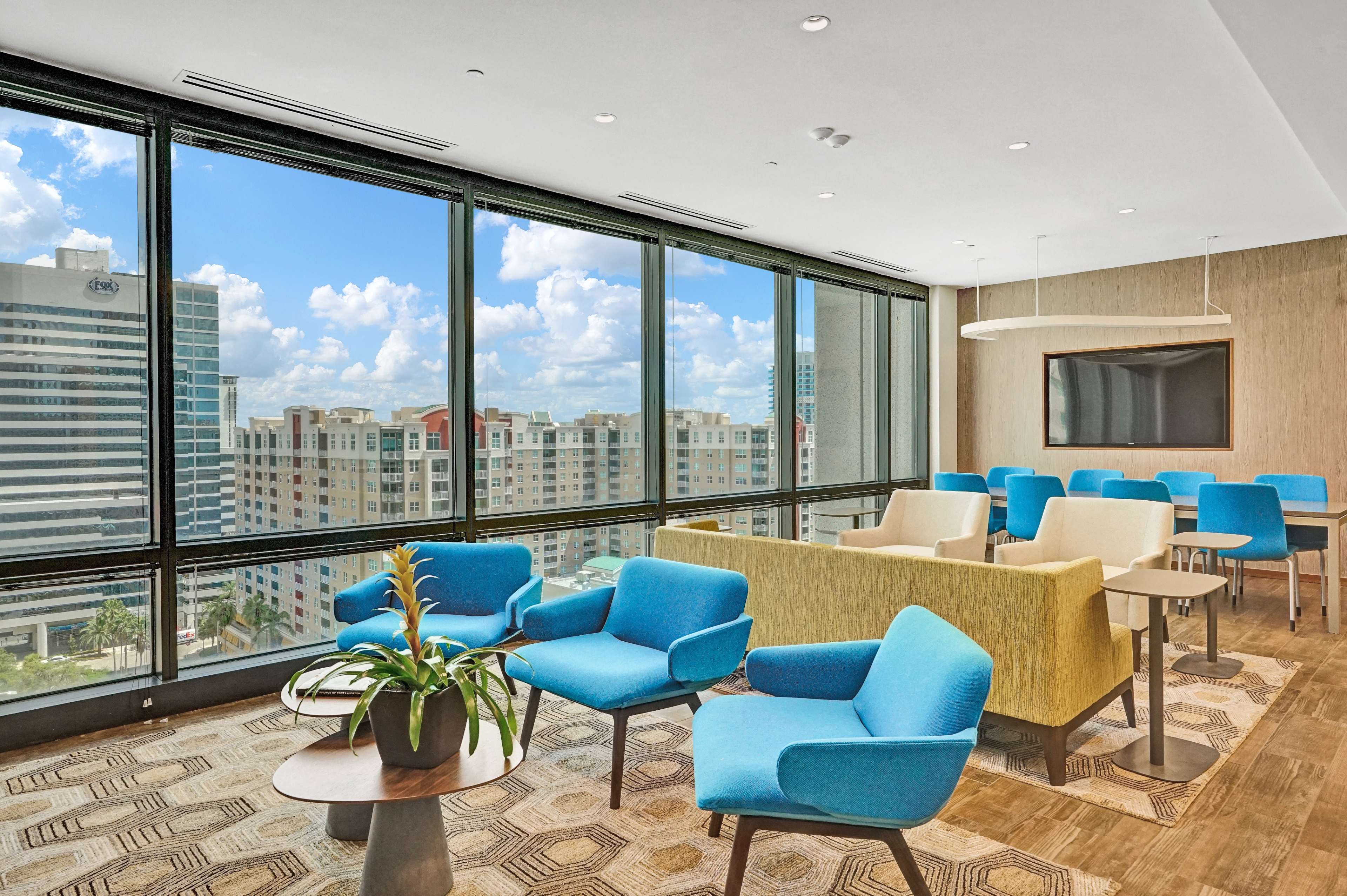 A modern office space features large windows with city views, blue and yellow seating arrangements, and wooden flooring.