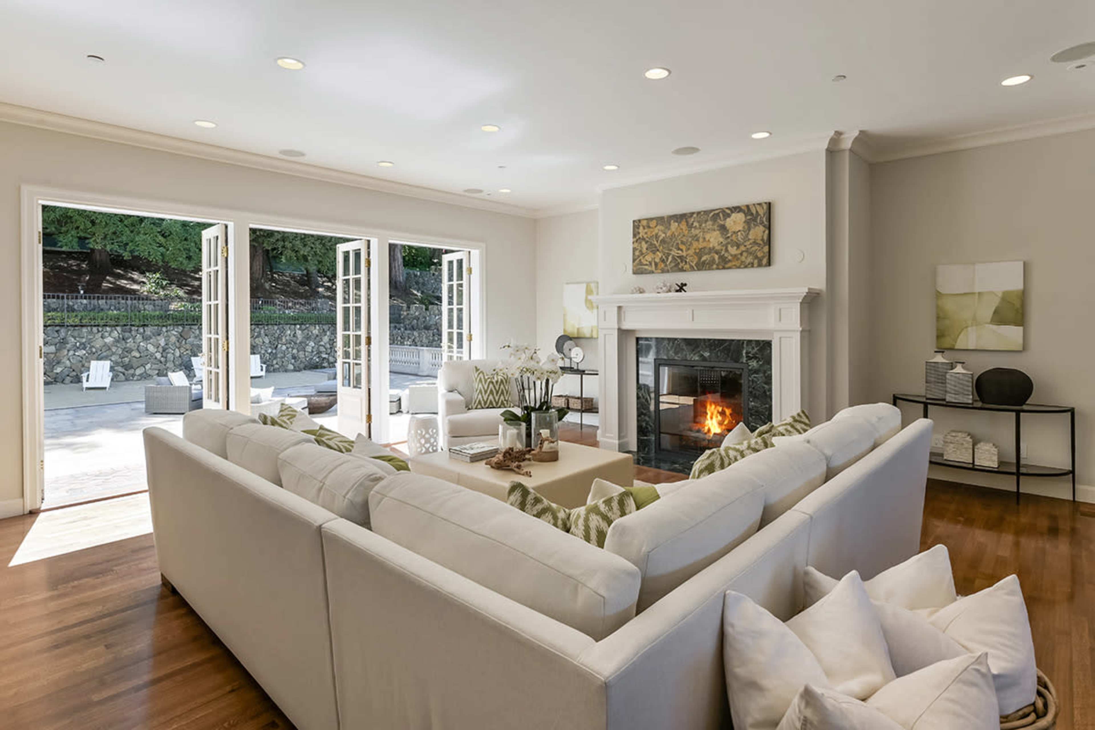 A spacious living room features a large sectional sofa facing a fireplace, with French doors opening to an outdoor patio.