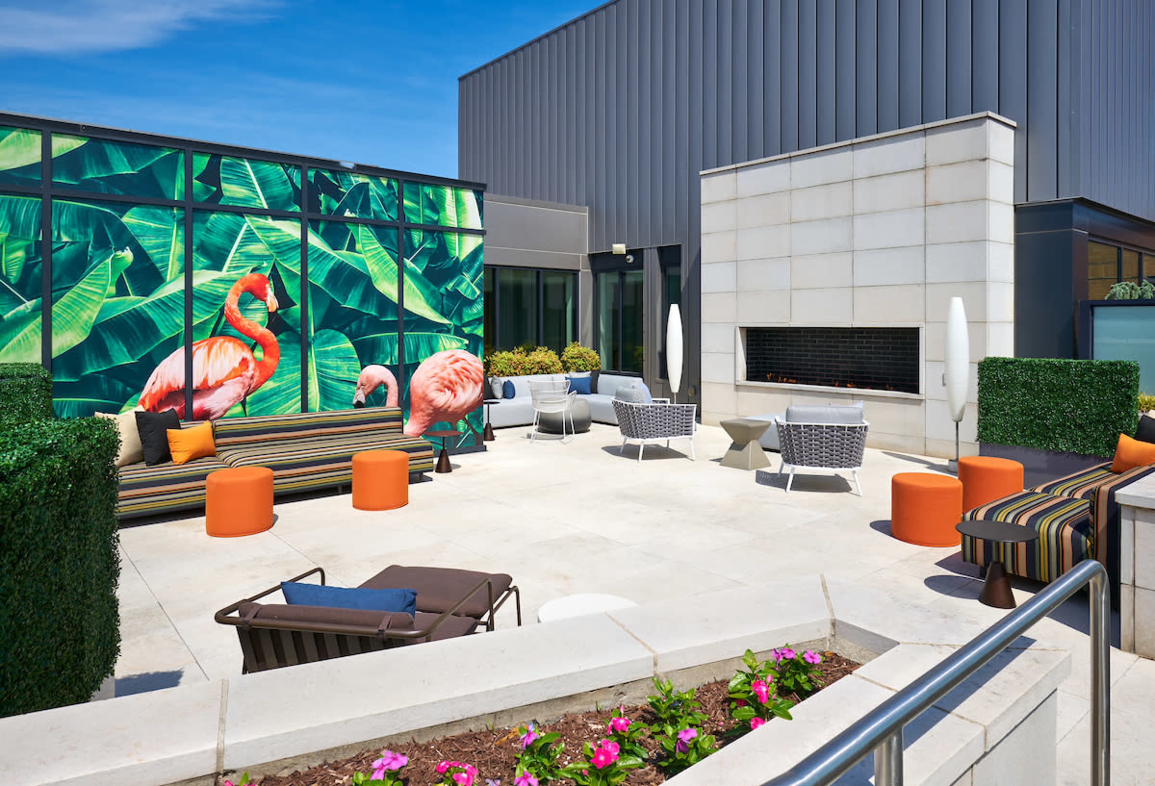 A rooftop patio featuring colorful seating, a decorative mural of flamingos, and a modern fireplace.
