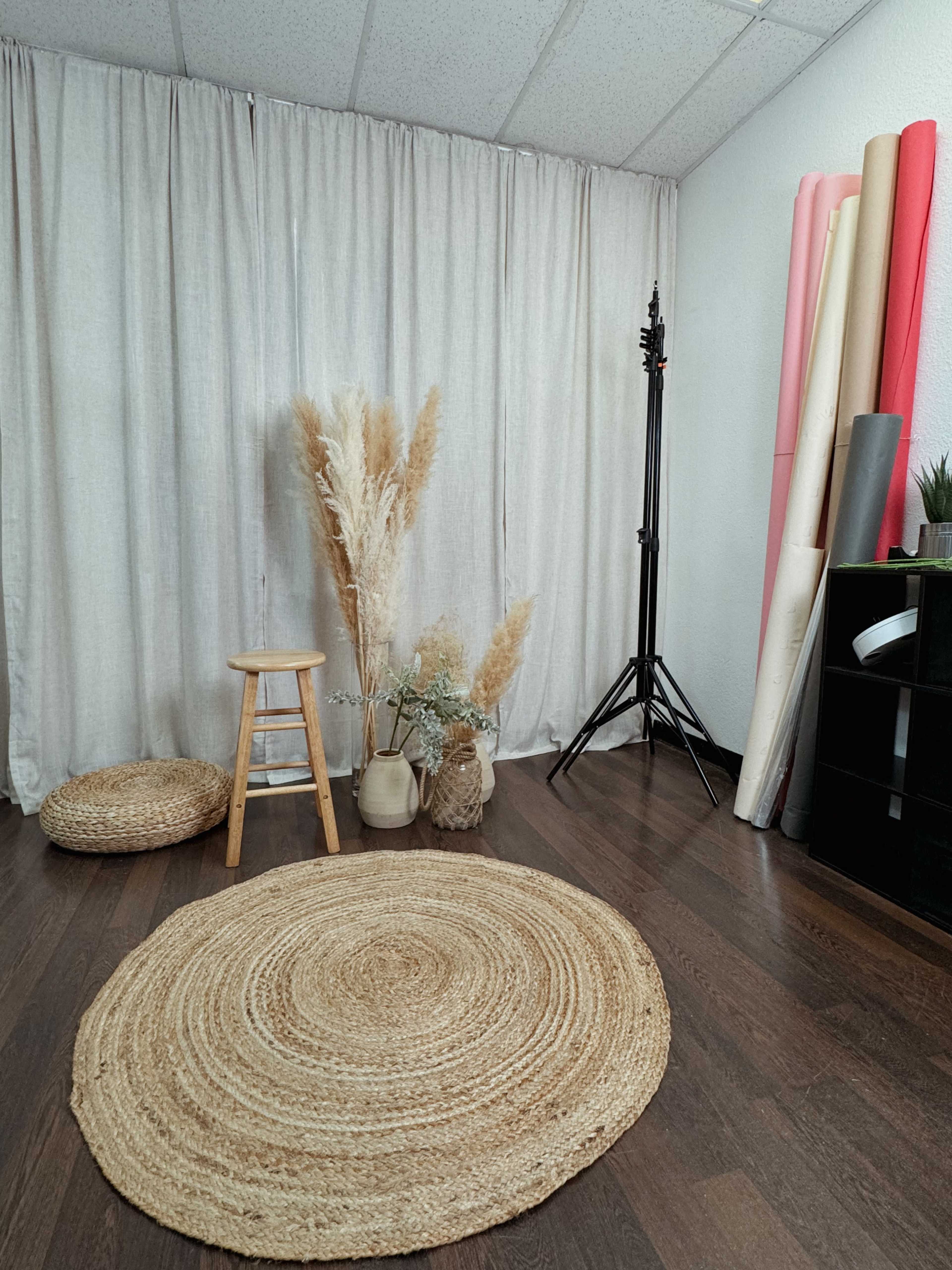 The image shows a photography studio with a stool, decorative plants, a large round rug, and rolls of colored paper against the wall.