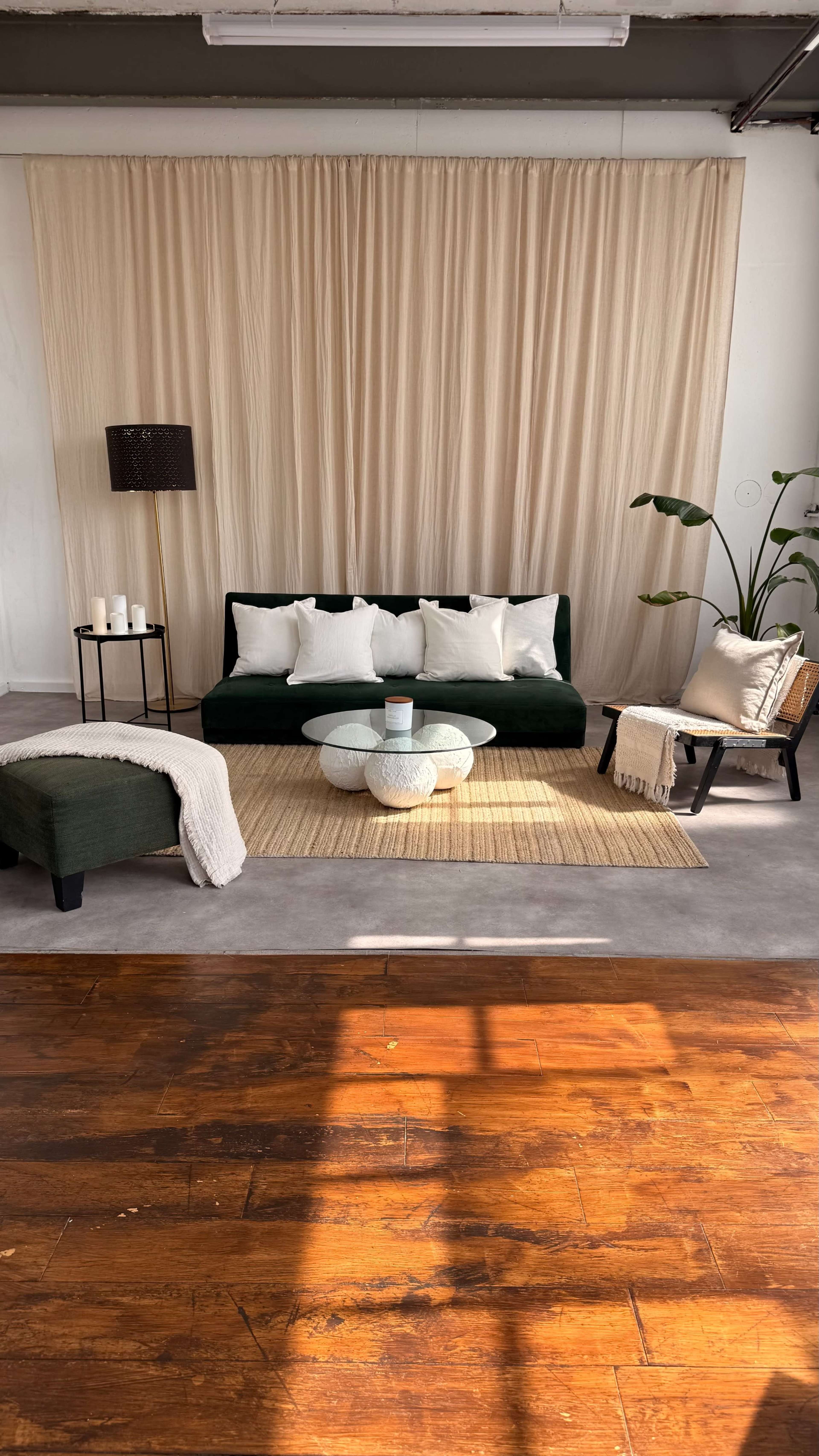 A modern living room features a green sofa with white cushions, a round glass coffee table, and a woven rug on a polished wooden floor, along with plants and decorative accessories.