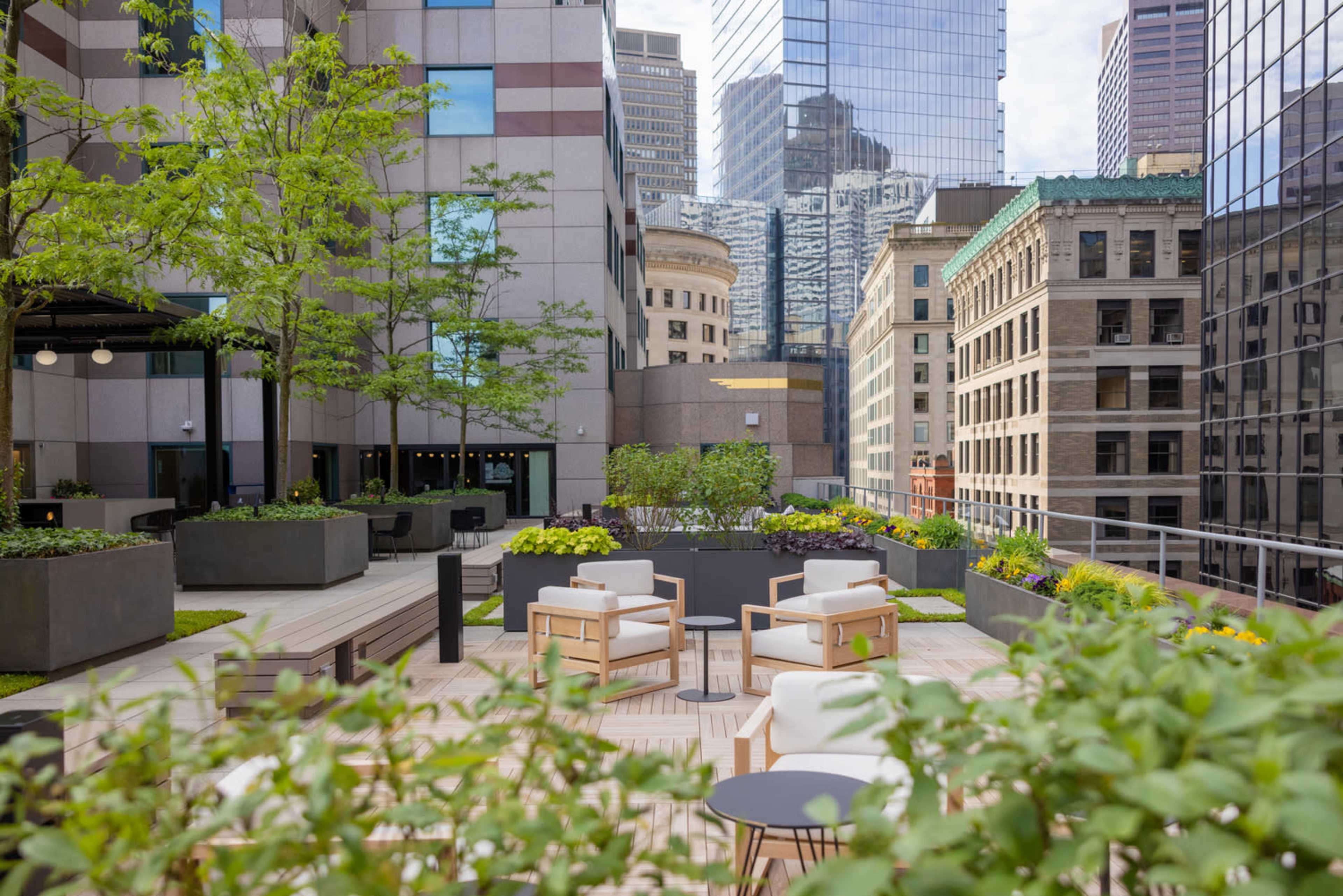 A modern rooftop garden with seating areas, surrounded by buildings in an urban setting.