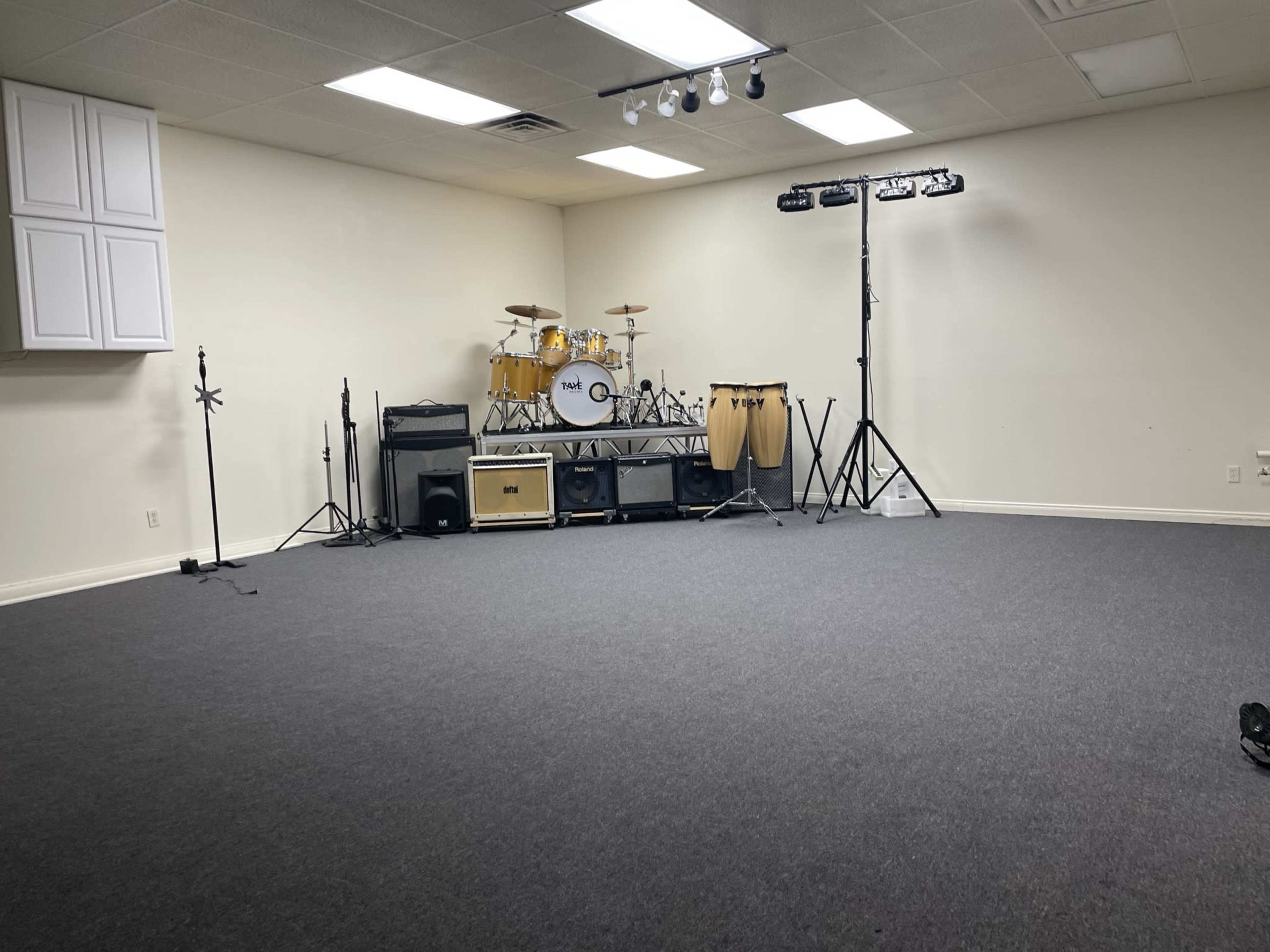 A spacious, empty room with a drum set and various musical equipment set up on a raised platform against the wall.