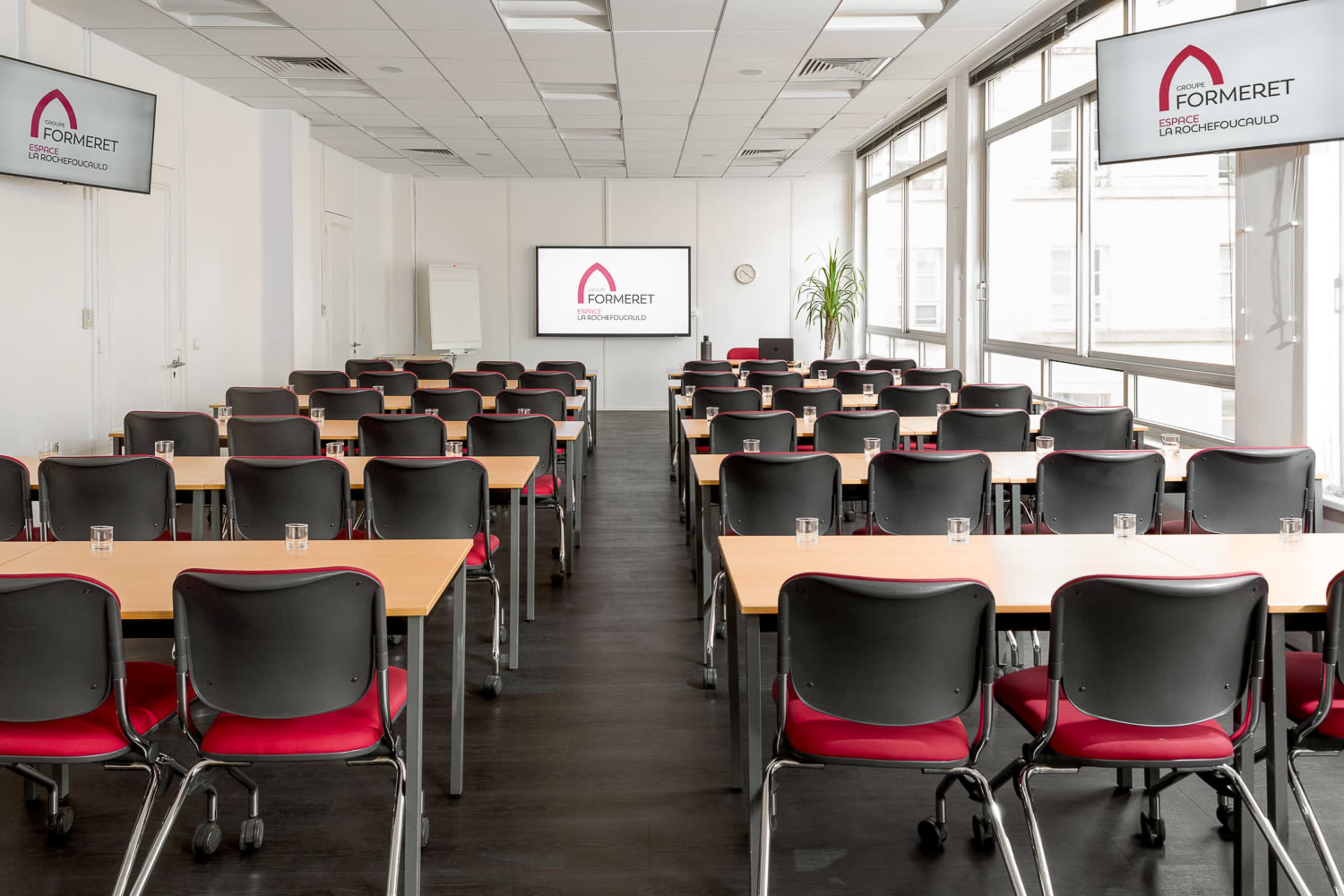 A conference room is set up with rows of tables and chairs facing two screens displaying the company logo.