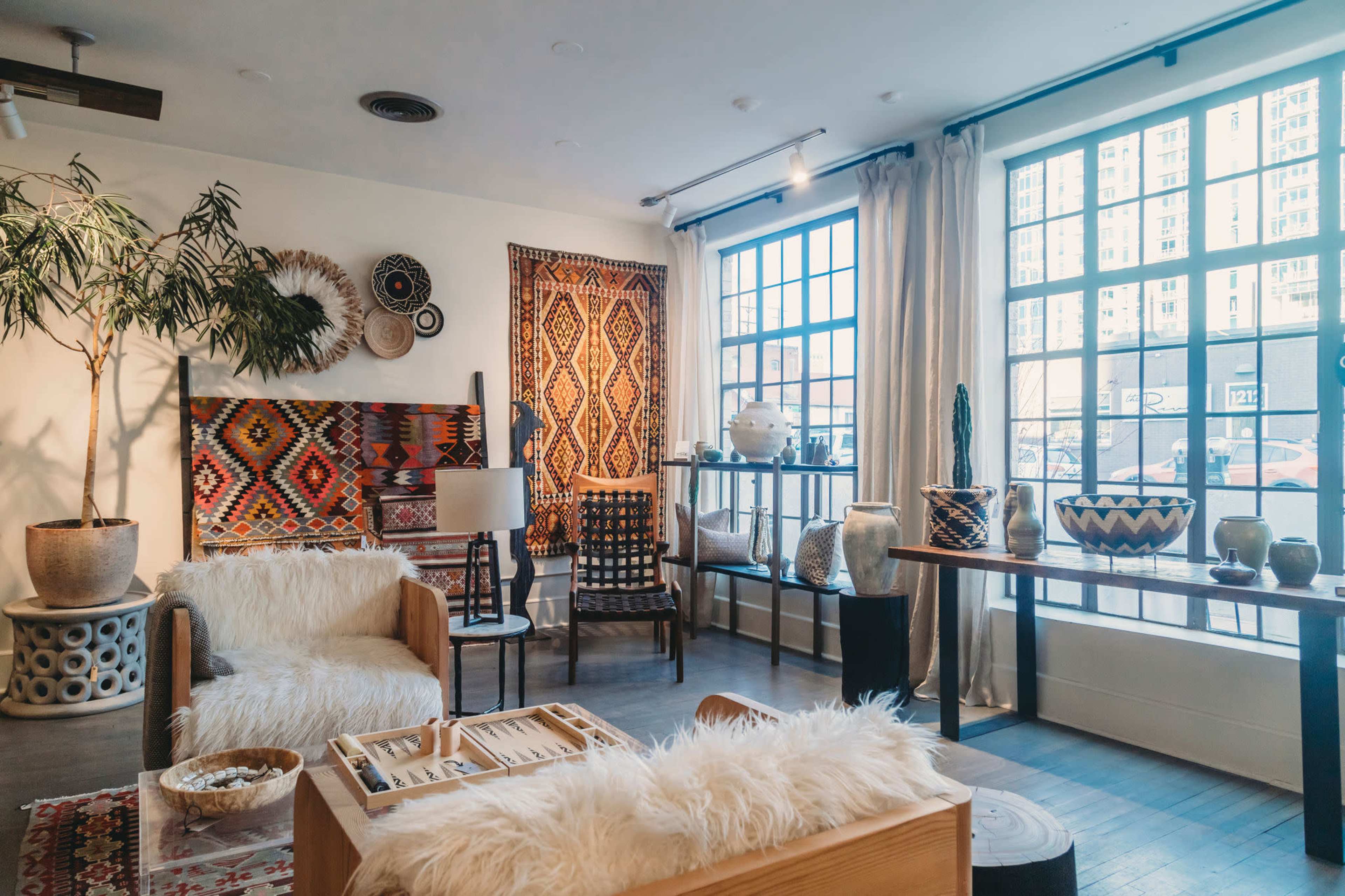 The image shows a well-decorated living room with patterned textiles on the walls, wooden furniture, and large windows allowing natural light.
