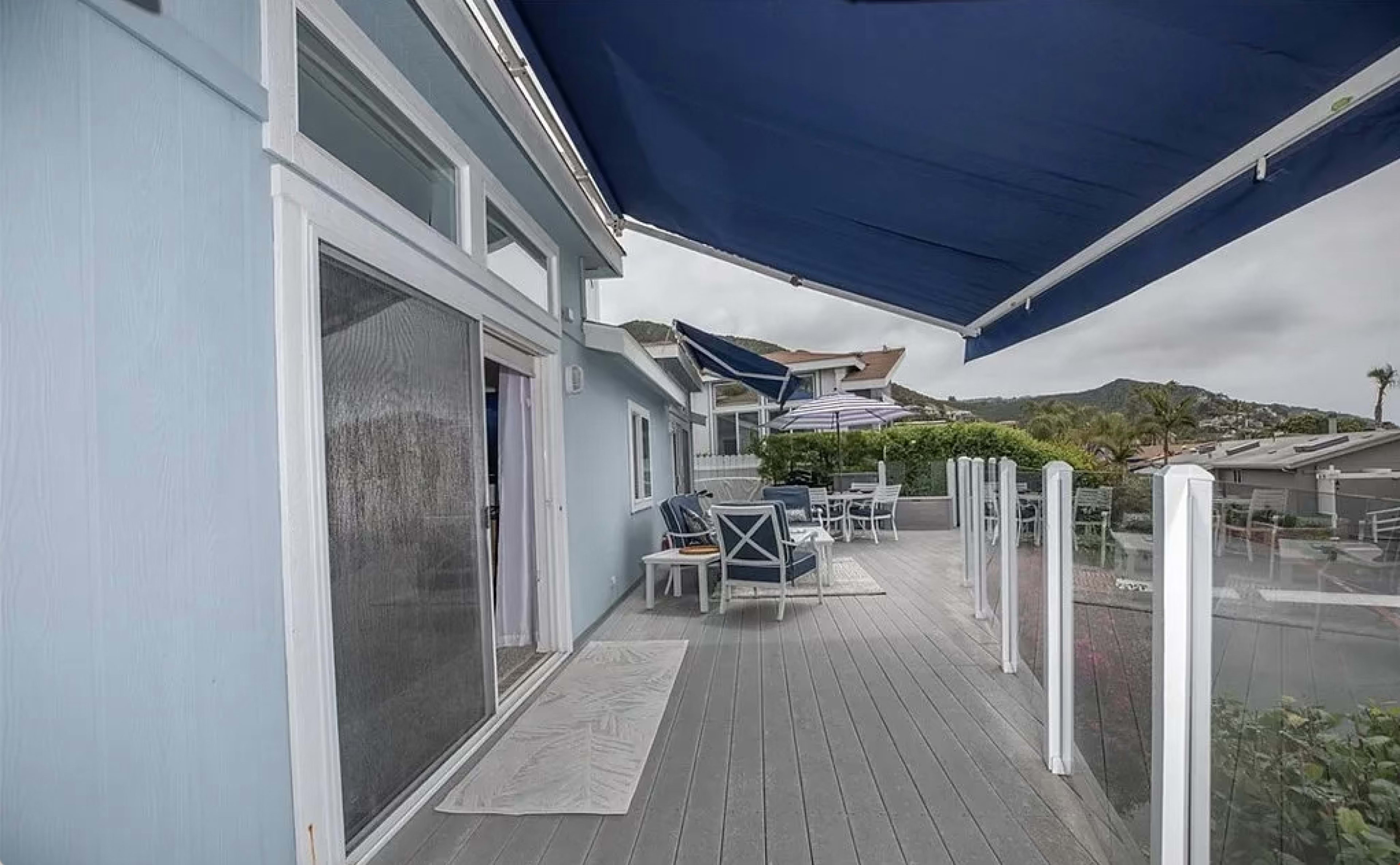 A patio with outdoor furniture and an awning, adjacent to a blue house and surrounded by greenery.