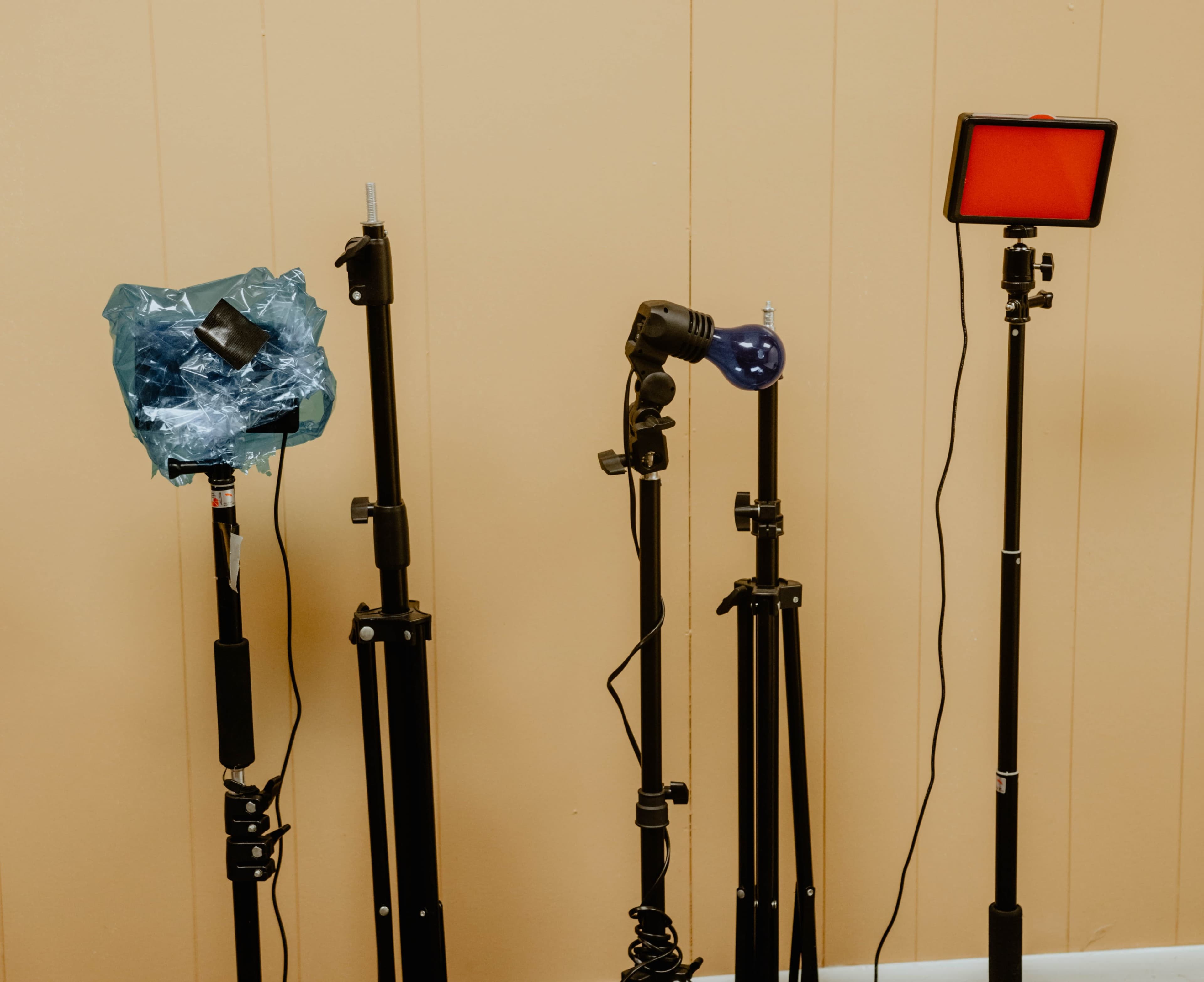 Four lighting stands of varying heights, each holding different types of light fixtures, against a beige wall.