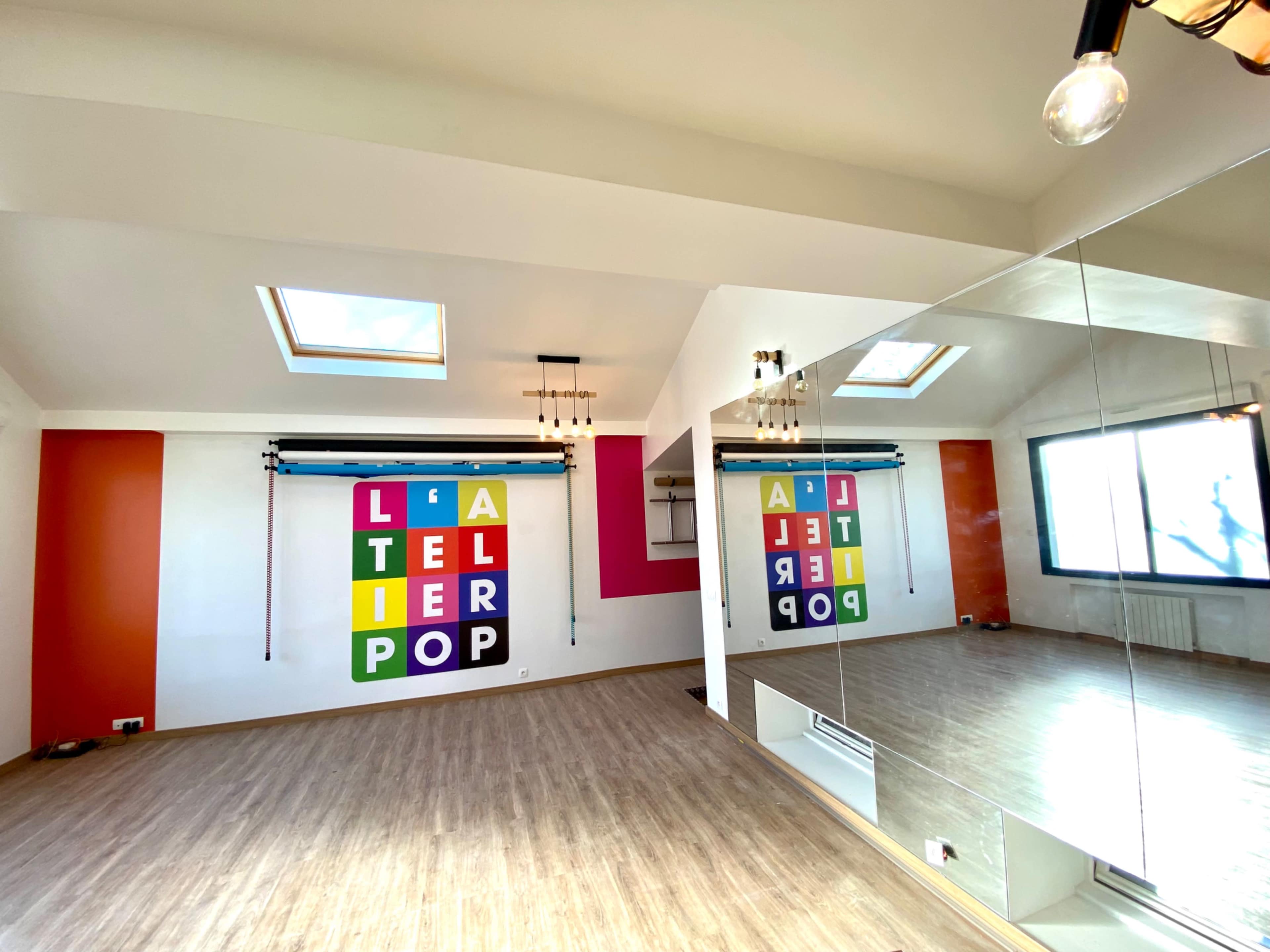 A bright, open studio space features colorful wall art, large mirrors, and skylights that allow natural light to fill the room.