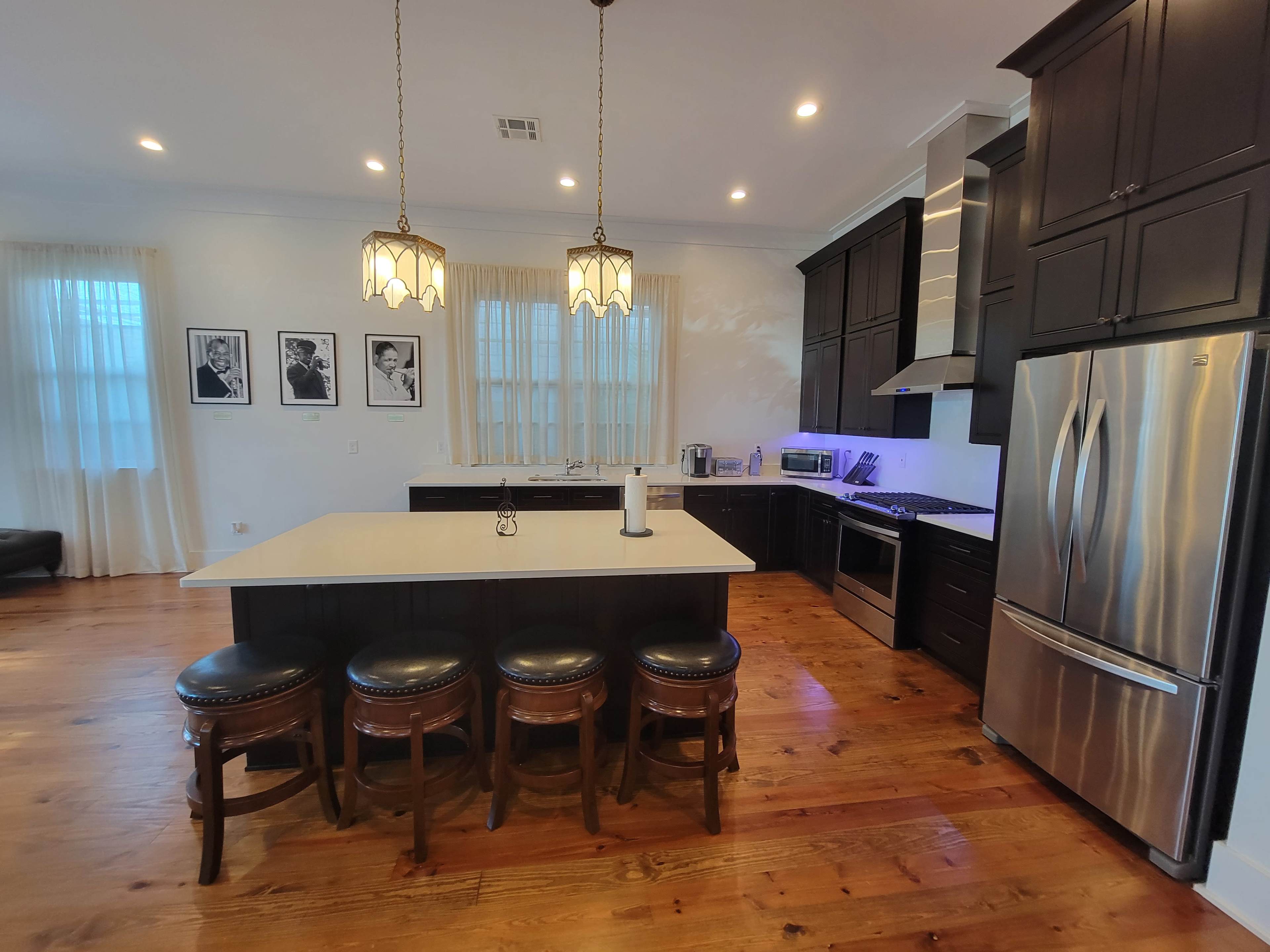 The kitchen features dark cabinetry, a large island with seating, stainless steel appliances, and pendant lighting.
