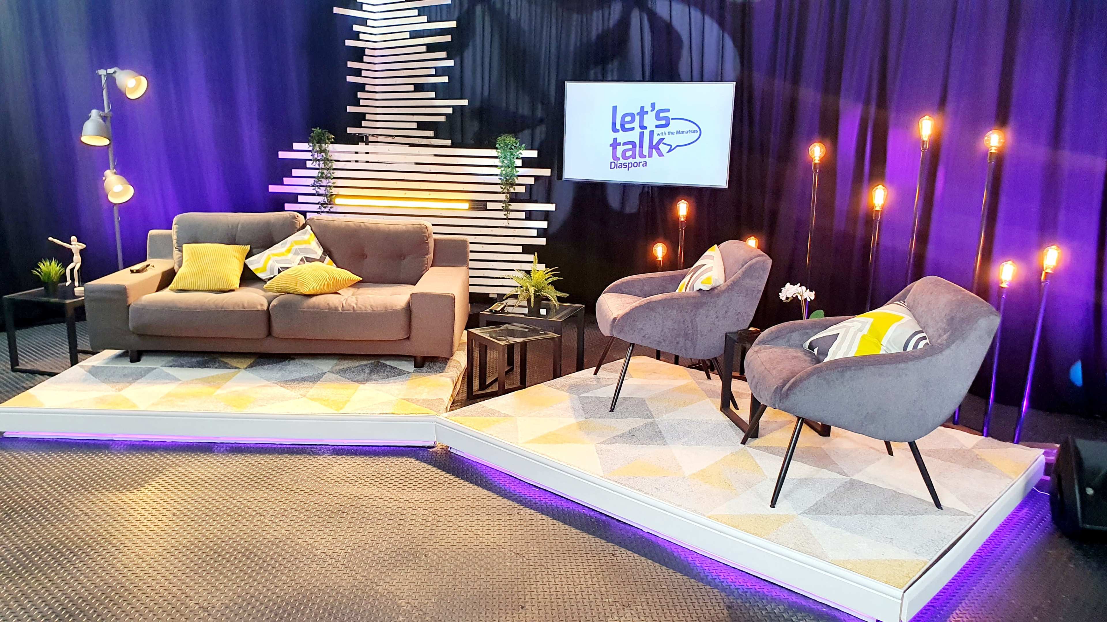 A modern talk show set featuring a sofa, two chairs, and decorative elements illuminated by soft lighting.