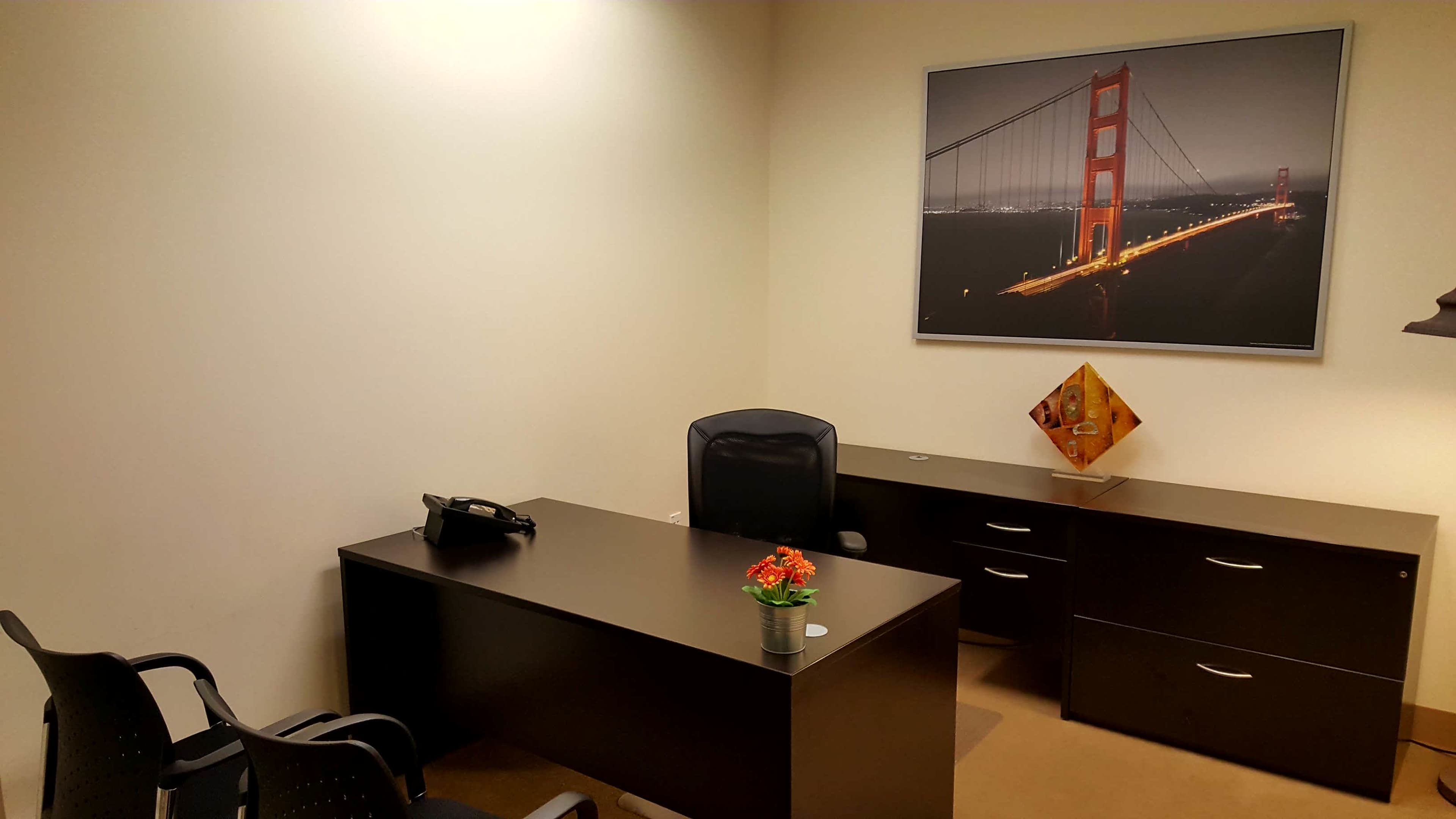 A neatly arranged office space featuring a desk, chair, and filing cabinet, with a large photograph of the Golden Gate Bridge on the wall.