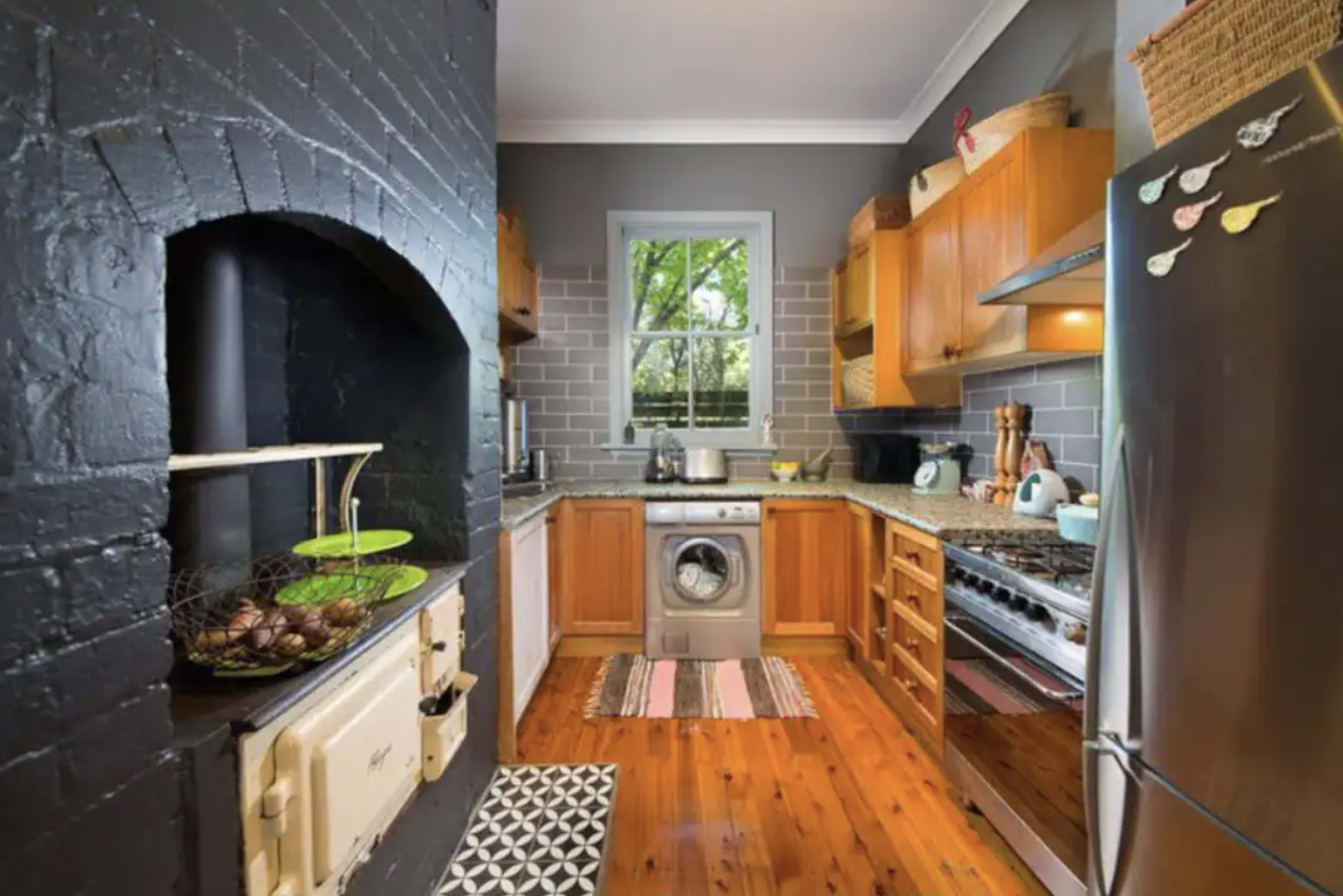 The kitchen features wood cabinets, stainless steel appliances, a washing machine, and a combination of black and gray walls, with natural light coming through a window.