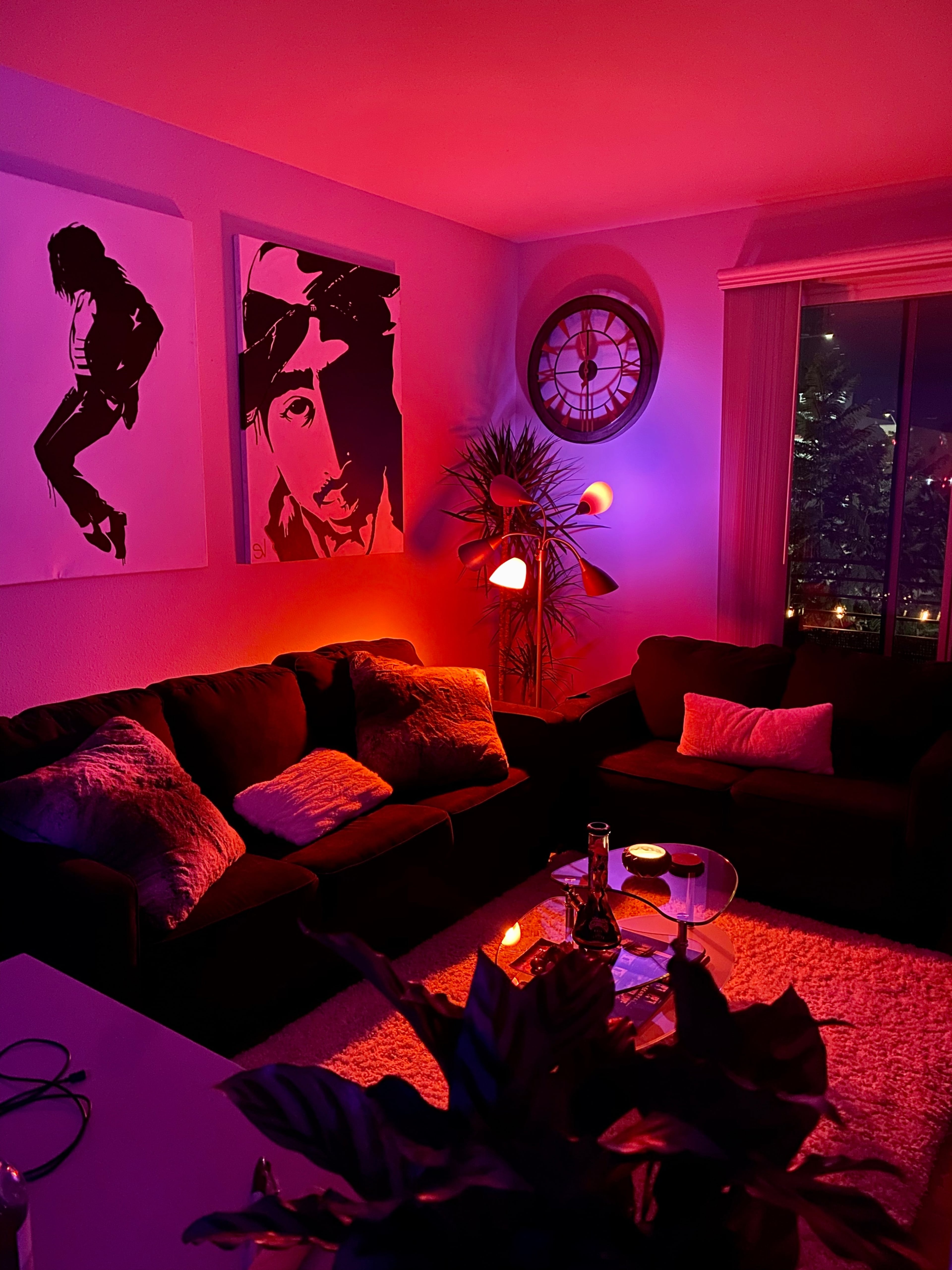 The living room features two large framed portraits on the wall and colorful ambient lighting, with a sofa and a glass coffee table.