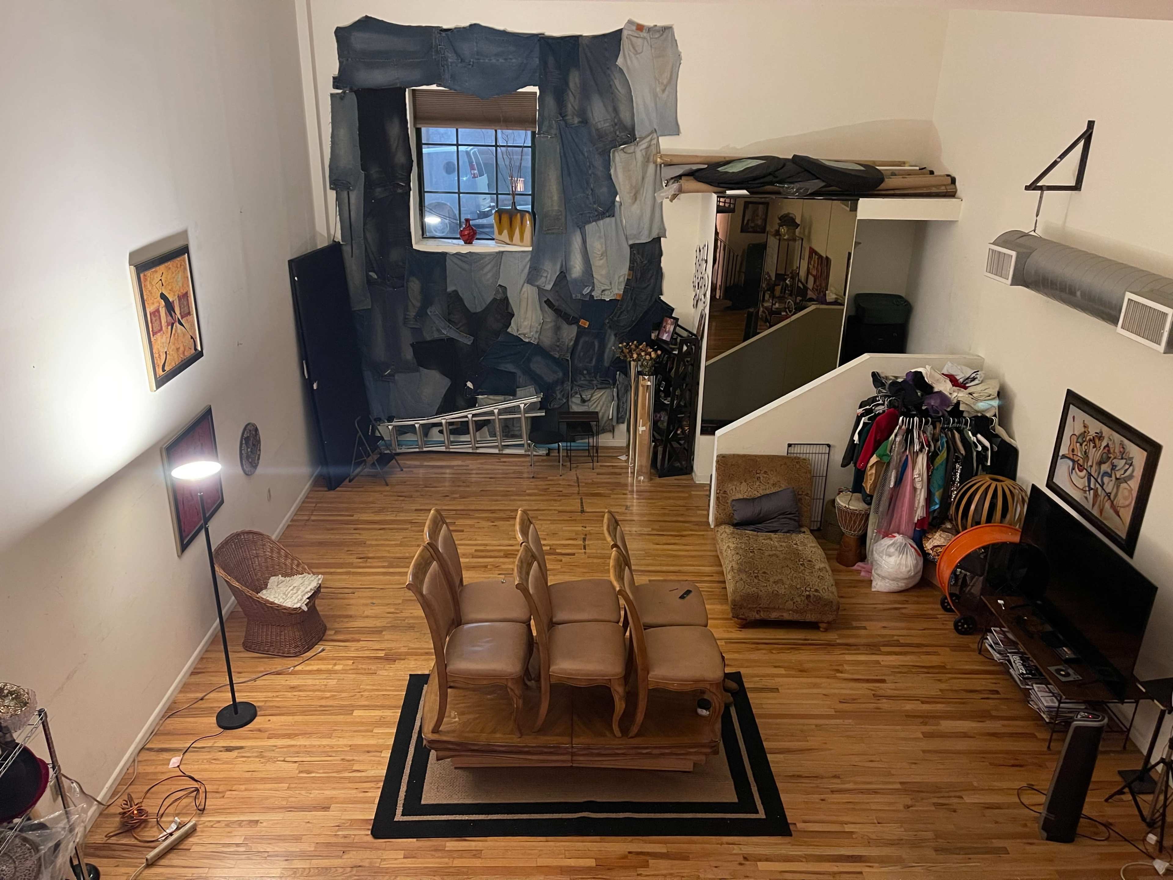 A spacious room with wooden flooring, featuring a seating area with chairs, a television, and an eclectic arrangement of decor items, including a large curtain made of fabric and a staircase leading to a second level.