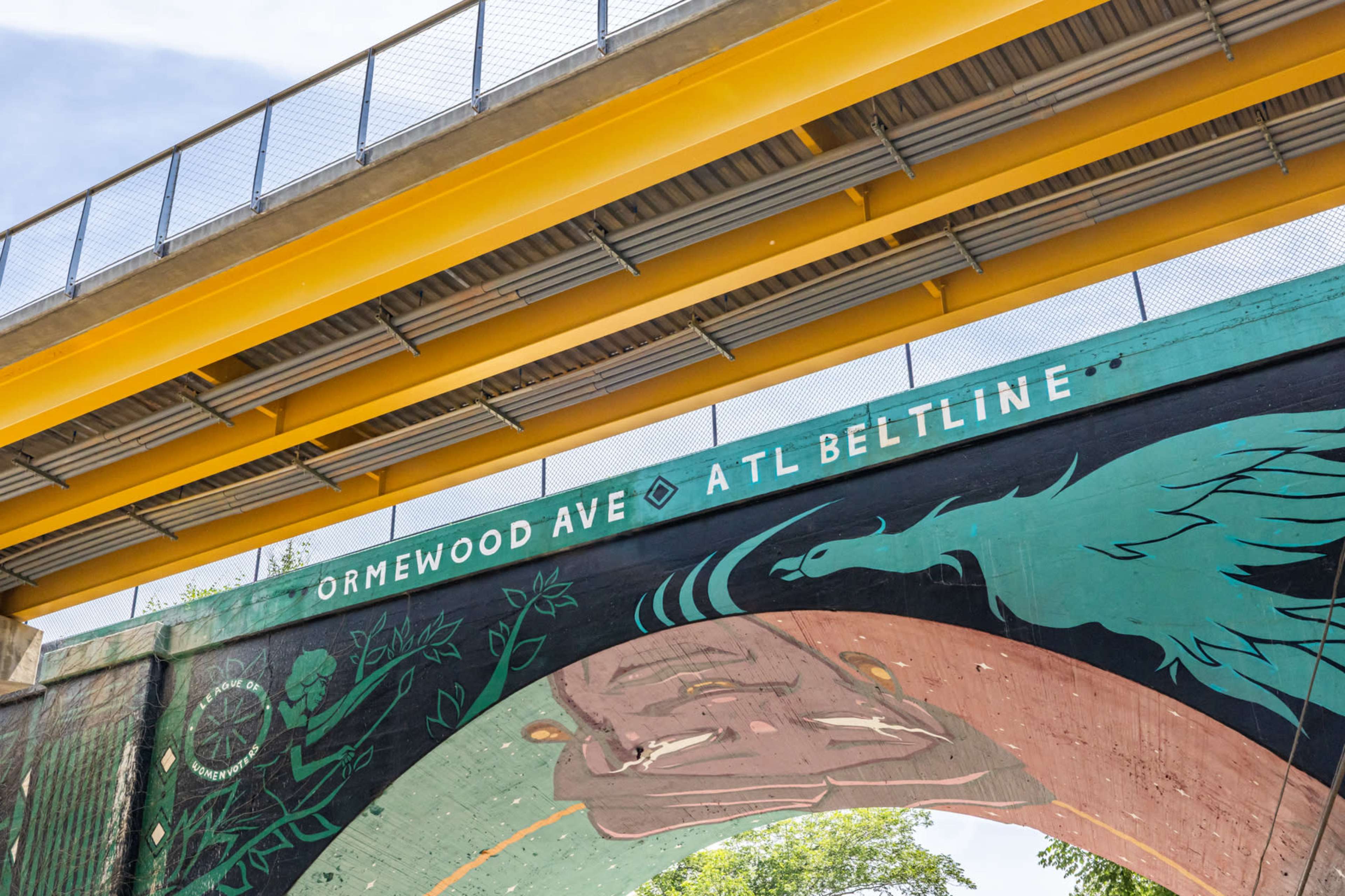 The image features a brightly colored elevated bridge with murals and signage indicating "Ormewood Ave" and "ATL Beltline."