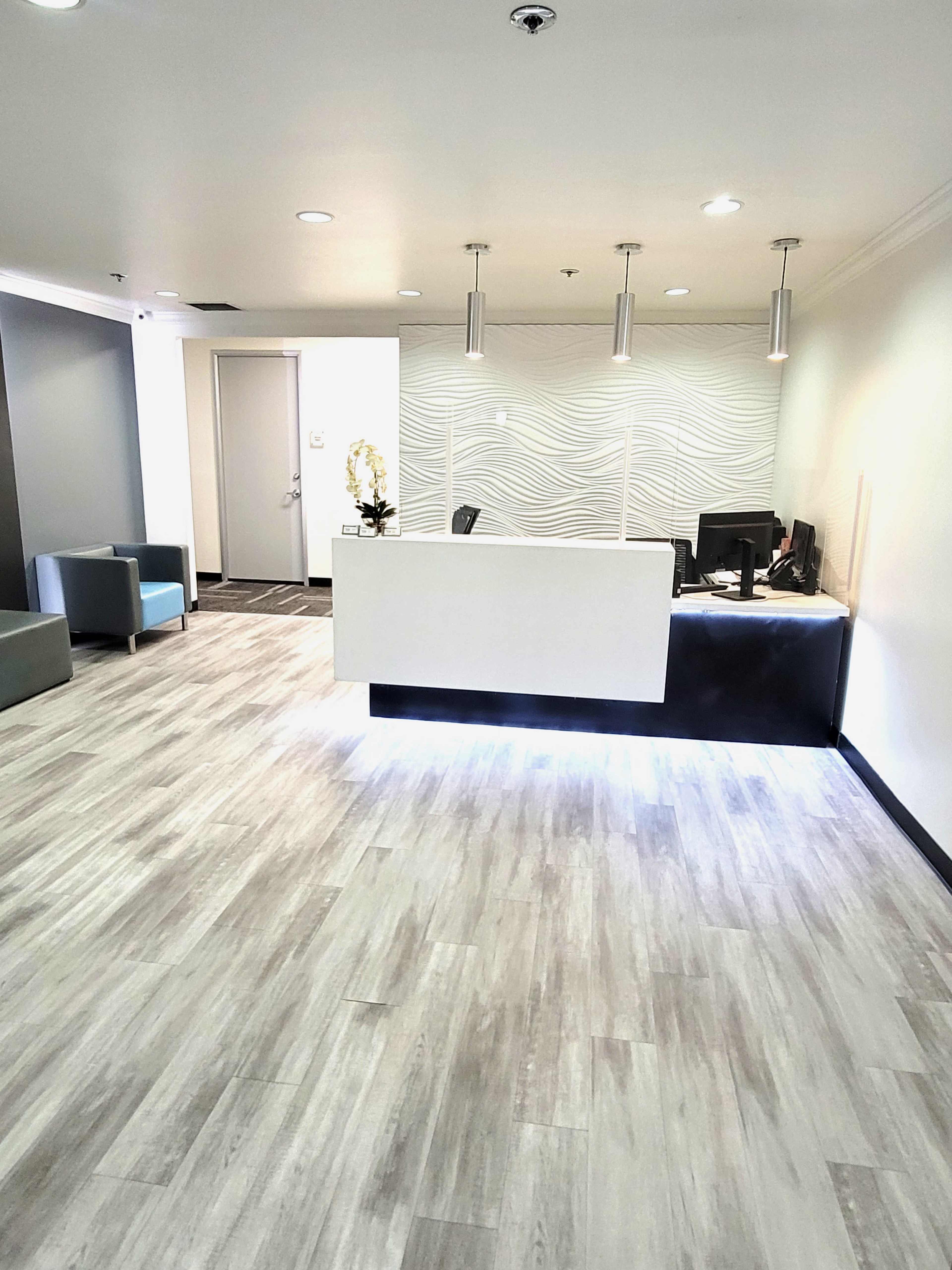 A modern reception area with a white front desk, a computer setup, and seating in the corners.