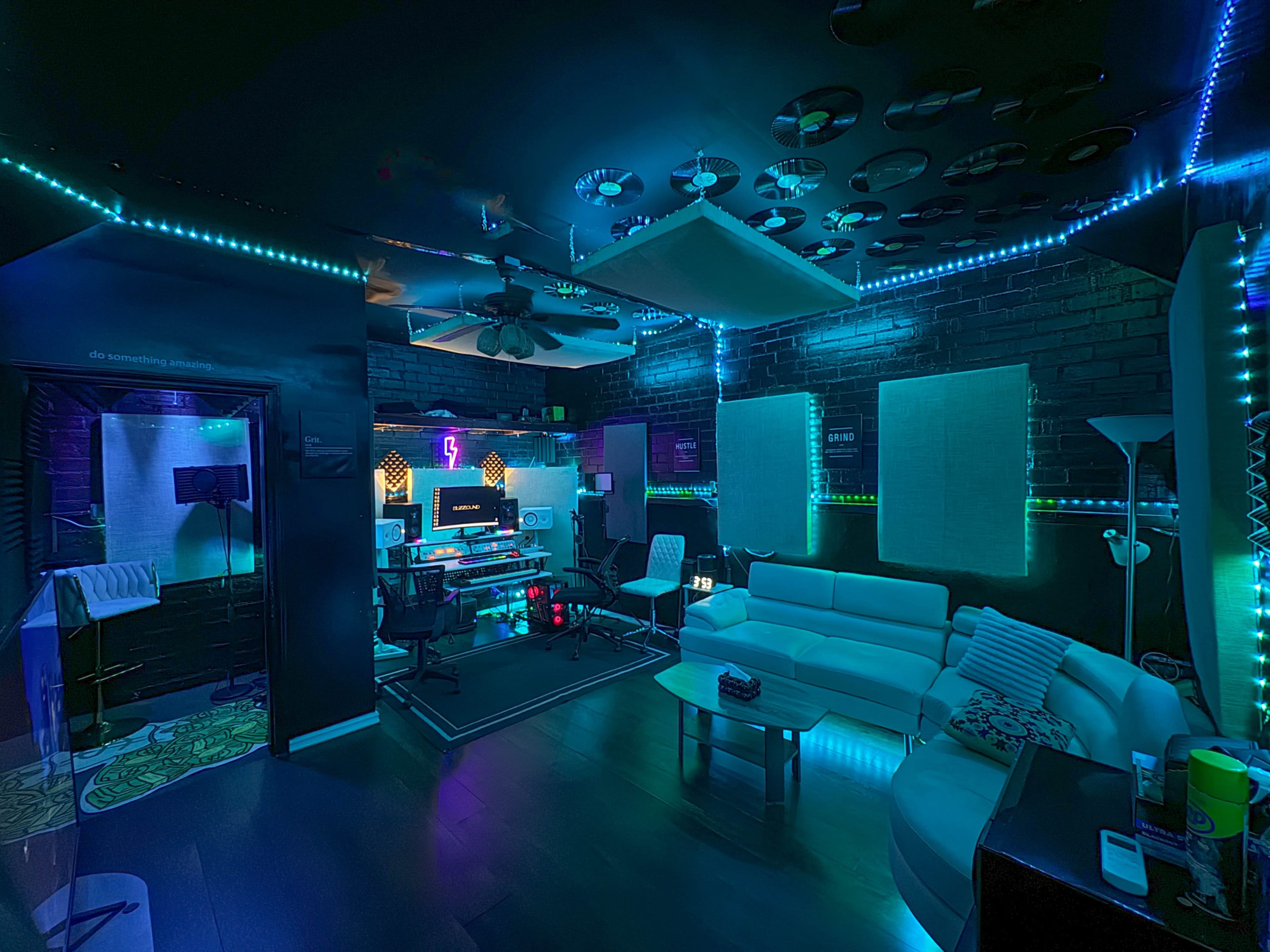 A music production studio features a mix of modern equipment, a white sofa, and ambient LED lighting against dark walls.