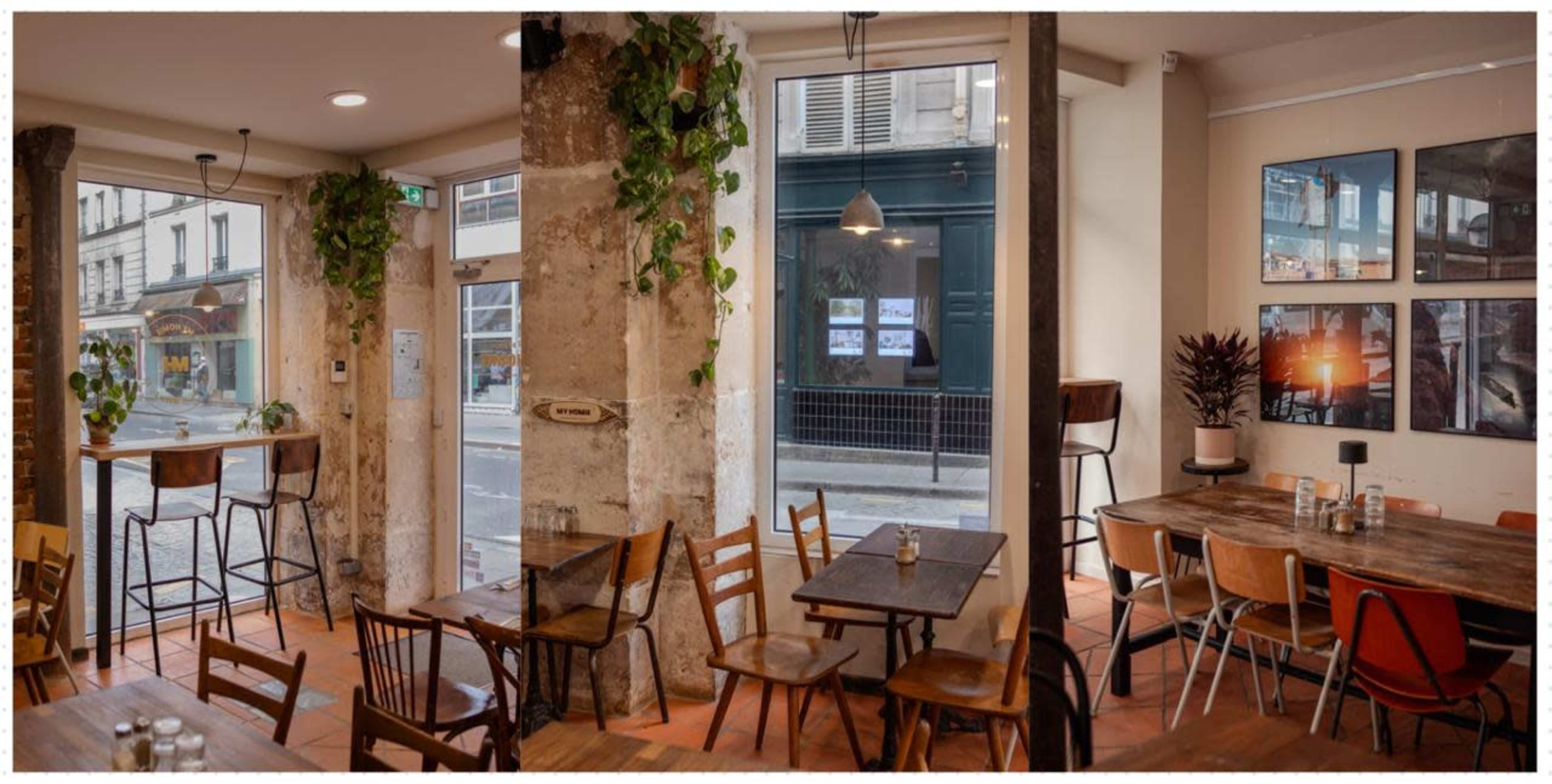 The image shows a cozy restaurant interior with wooden tables and chairs, large windows displaying a city street, and plants adorning the pillars.