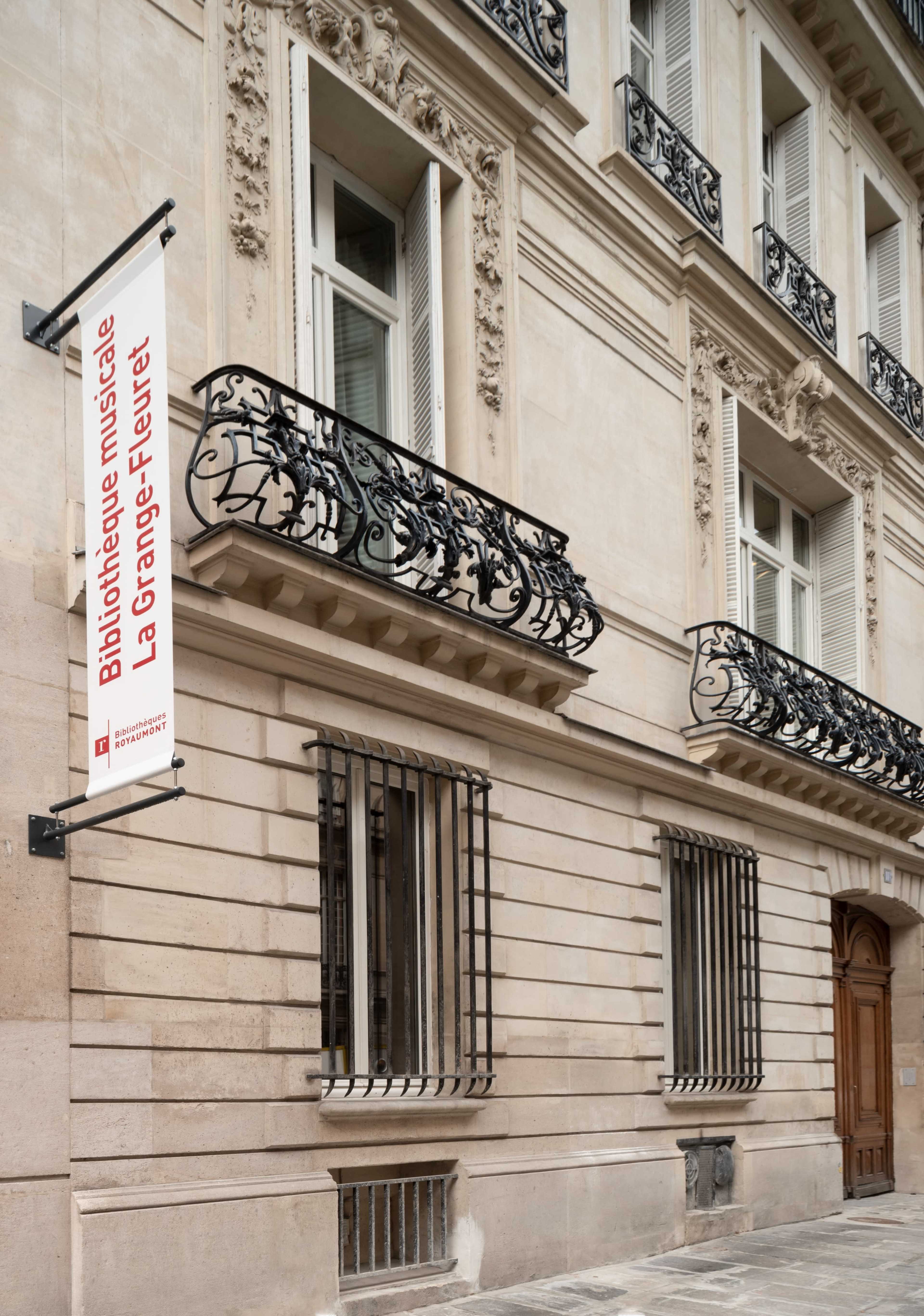 The image shows the exterior of the "Bibliothèque musicale La Grange-Fleuriet," featuring a banner and ornate wrought-iron balconies on a stone building facade.