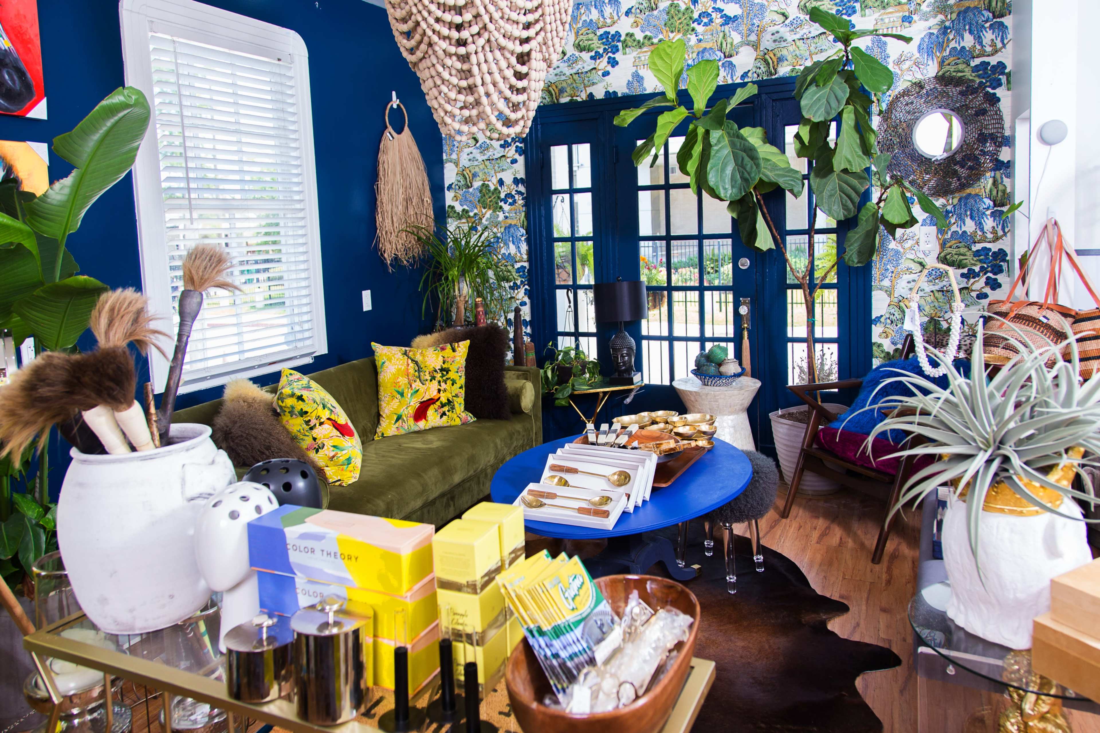 The image showcases a vibrant living space featuring a mix of plants, decorative elements, and colorful furnishings against a bold wallpaper backdrop.