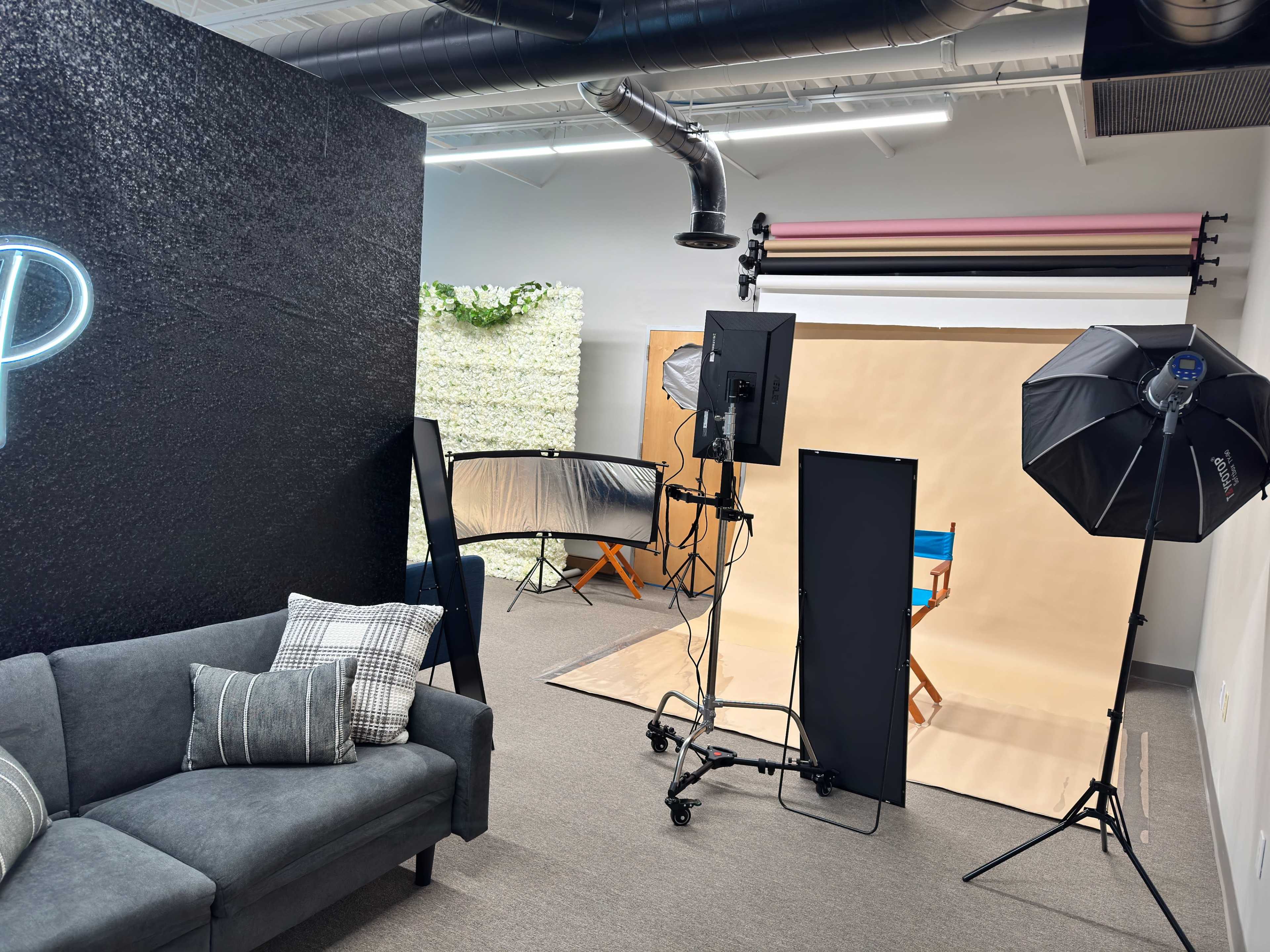 The image shows a photography studio setup with a couch, backdrop stands, and lighting equipment arranged for a photo shoot.