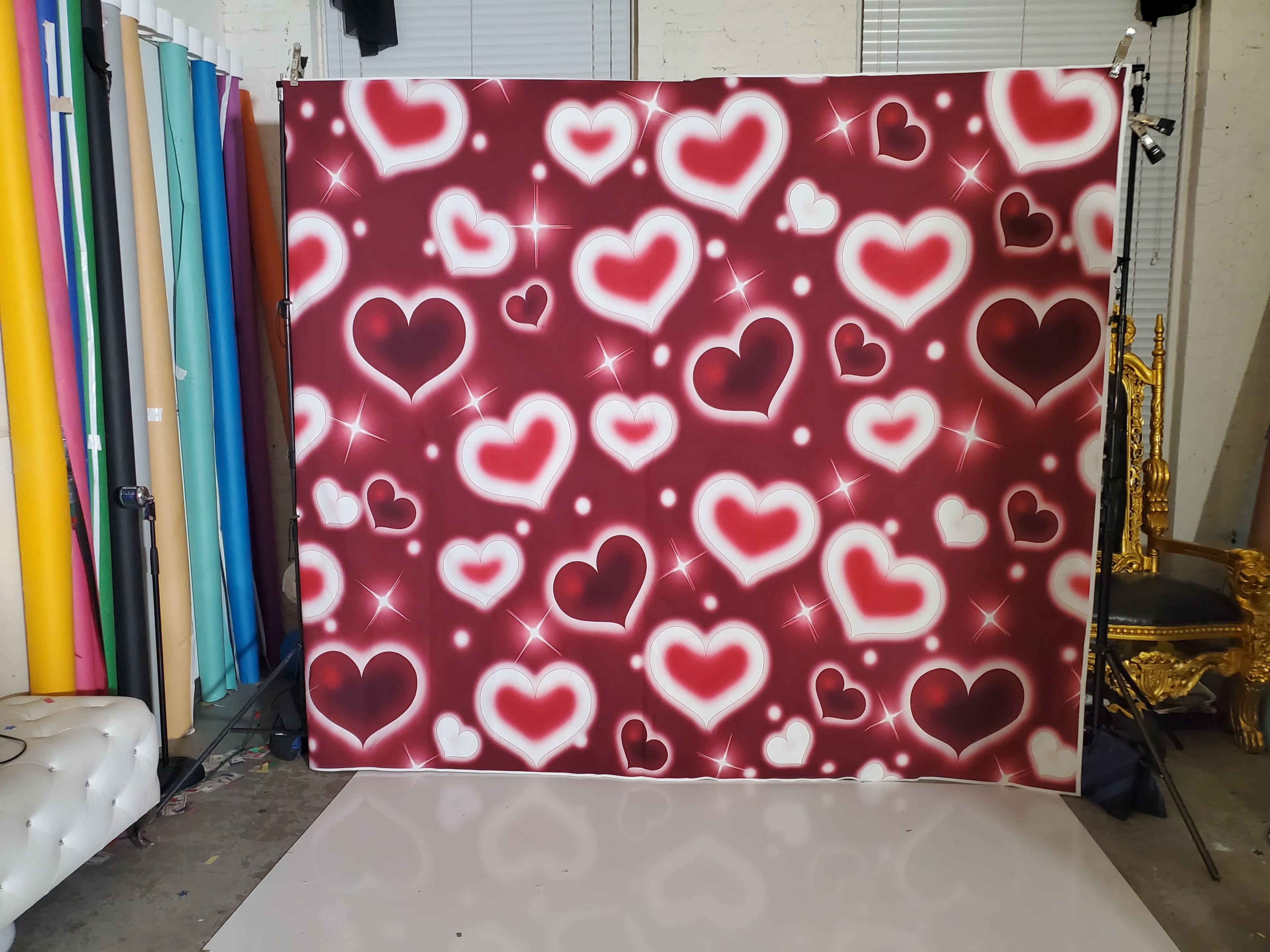 The image shows a backdrop featuring various hearts on a red background, with a shiny, star-like effect, set in a studio environment.