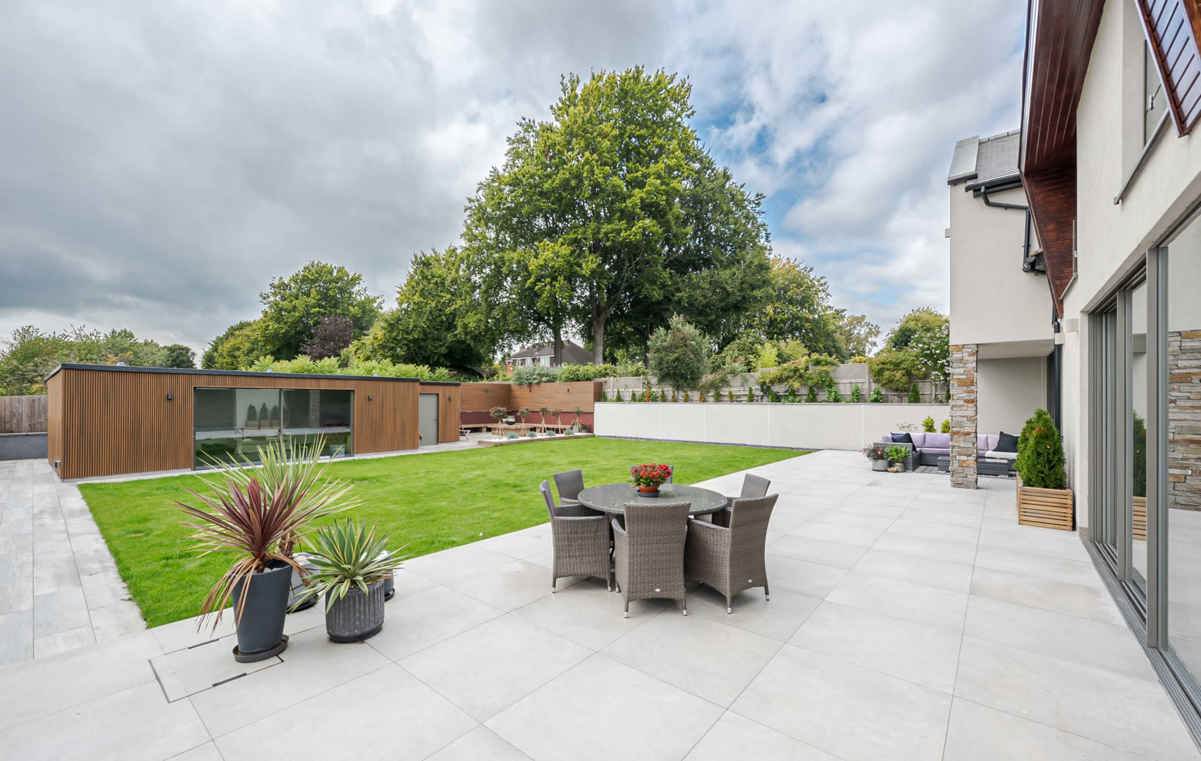 A modern backyard features a patio with dining furniture, a manicured lawn, and a contemporary shed among landscaped greenery.