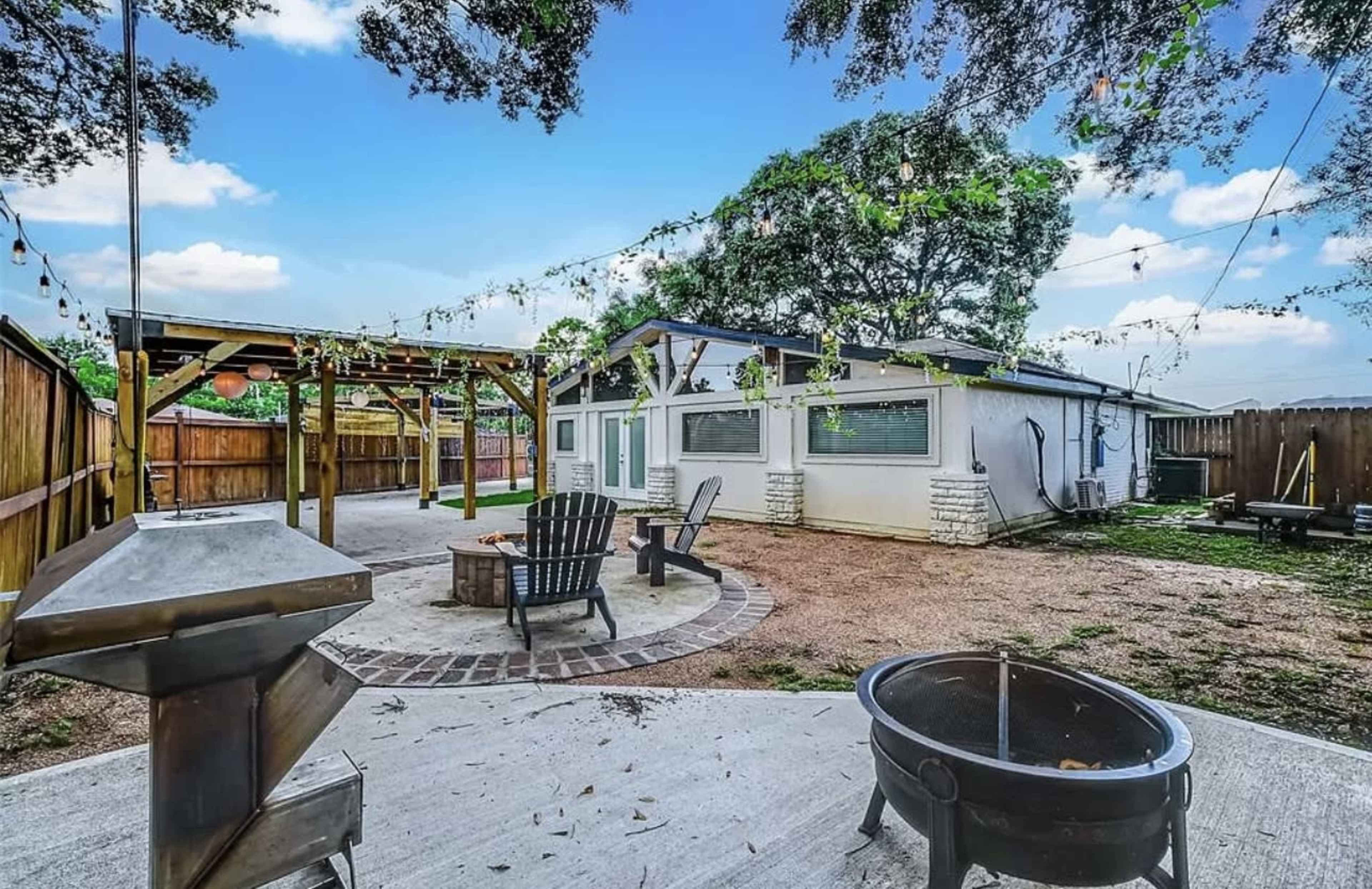 The image shows a backyard with a fire pit, seating area, and a wooden structure against a house.