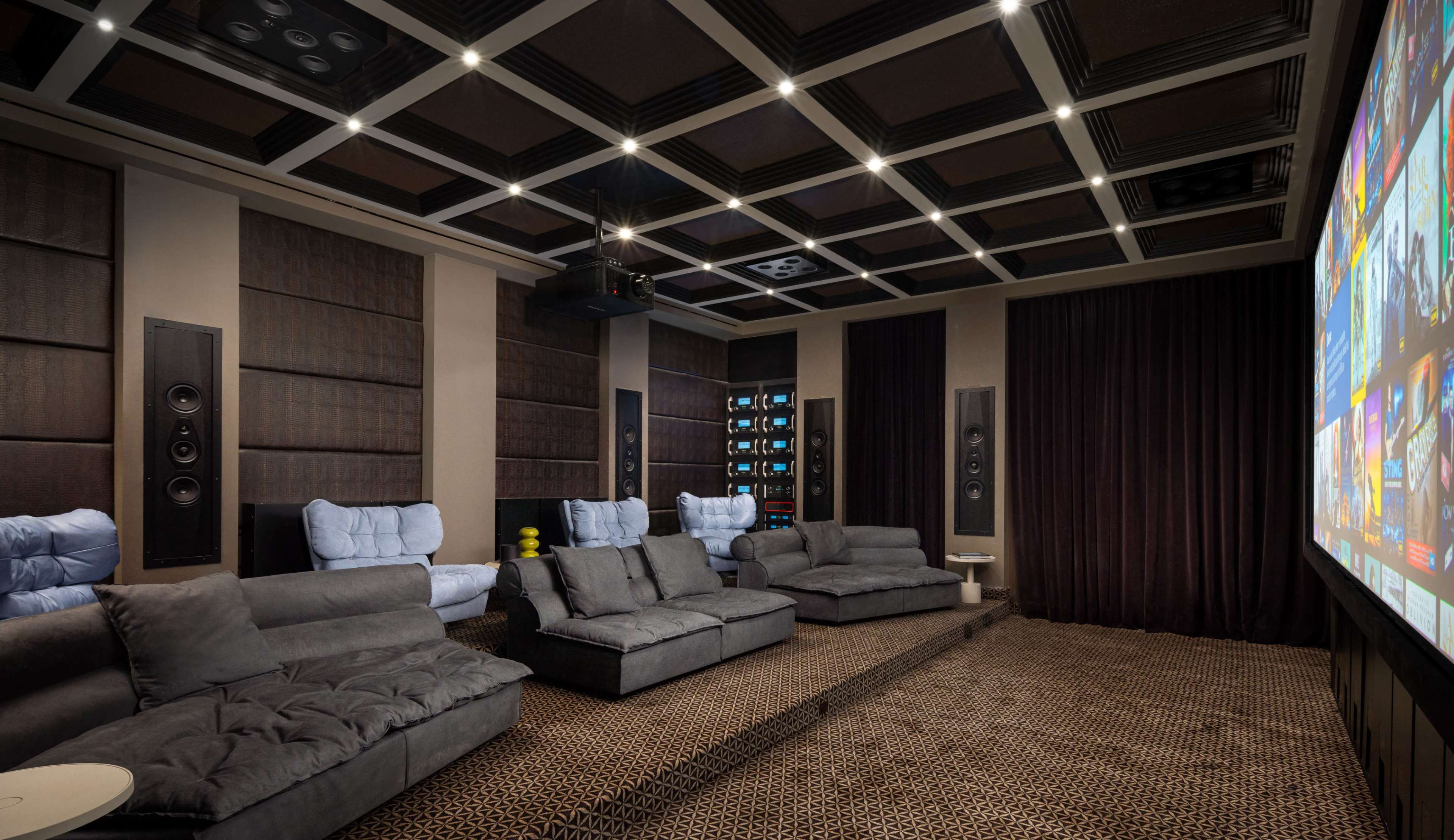 The image shows a modern home theater with plush seating, a large screen, and speaker systems on either side of the room.