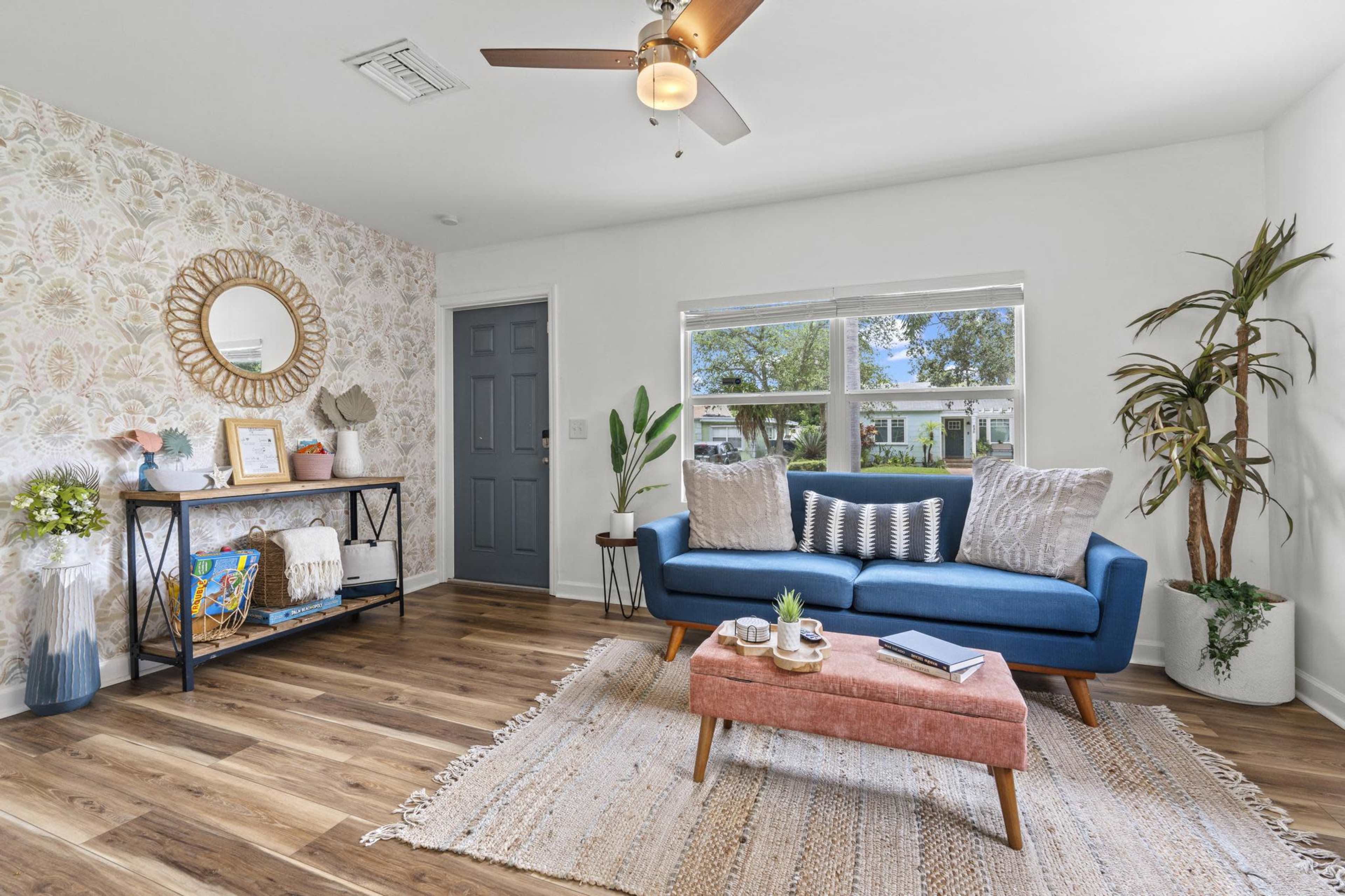 The room features a blue sofa, a wooden coffee table, and a decorative wall with floral wallpaper and a round mirror.