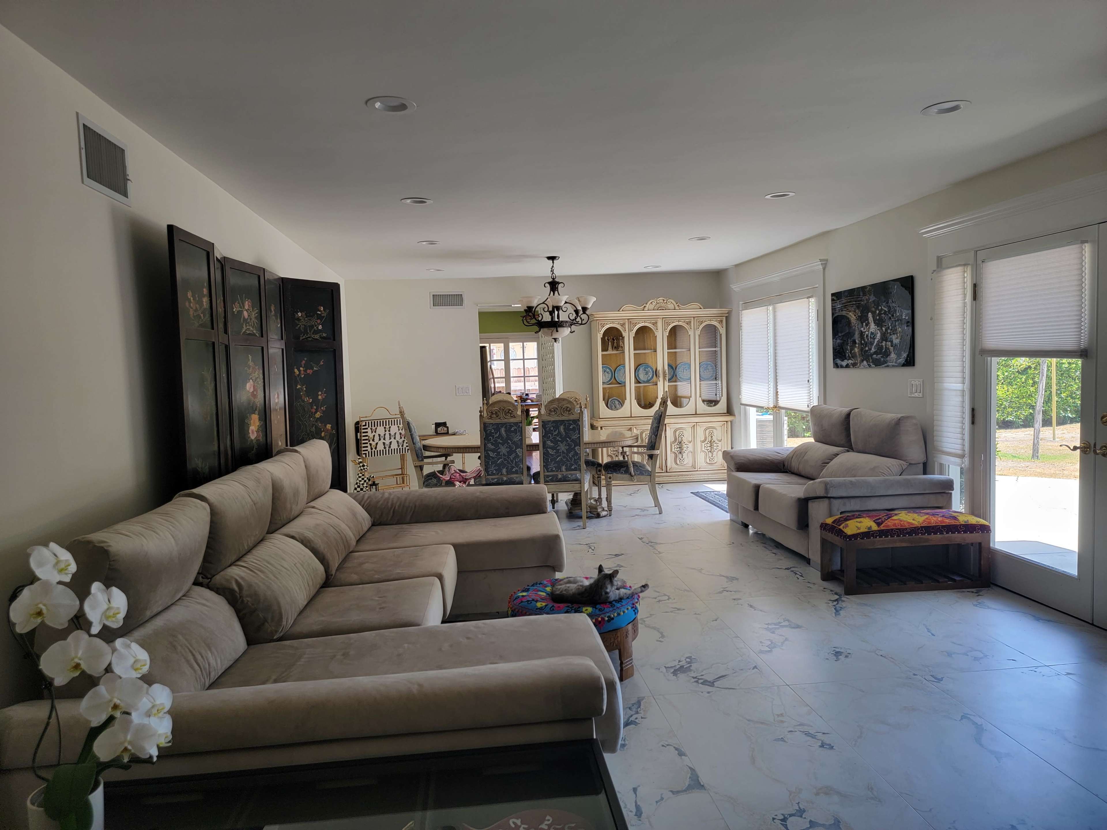The room features a light-colored living space with a sectional sofa, a dining area with ornate furniture, and large windows that provide natural light.