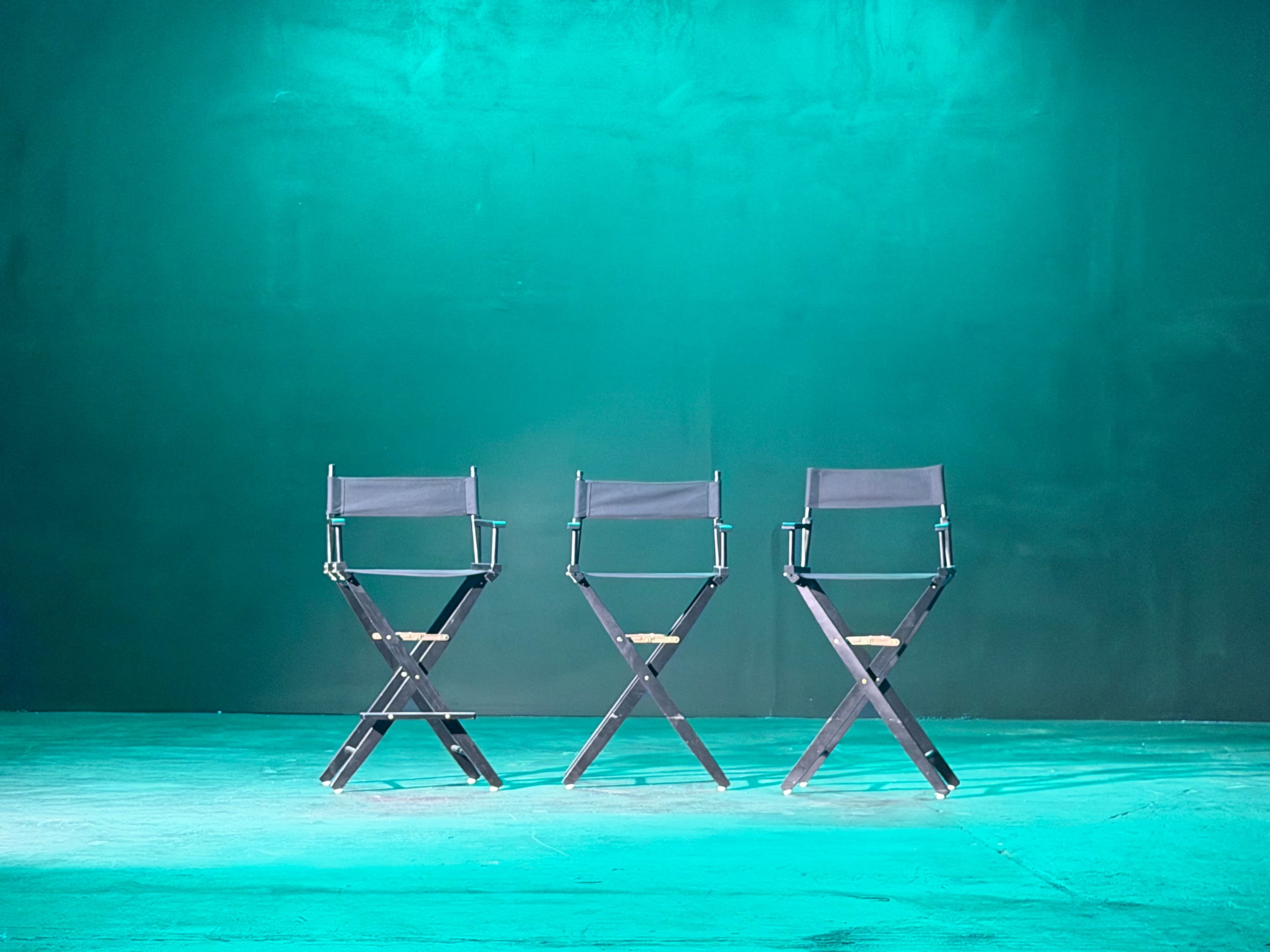 Three black director's chairs are positioned in a row against a teal backdrop.