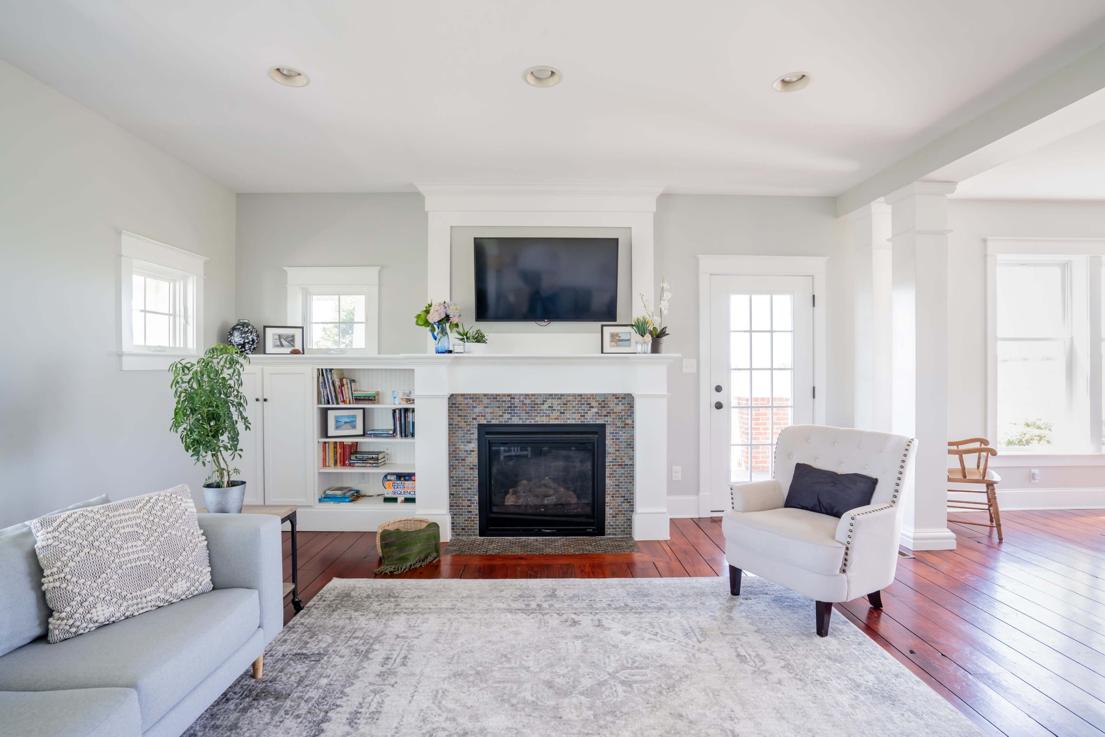 A light-filled living room features a fireplace with a television above, surrounded by bookshelves and seating areas.