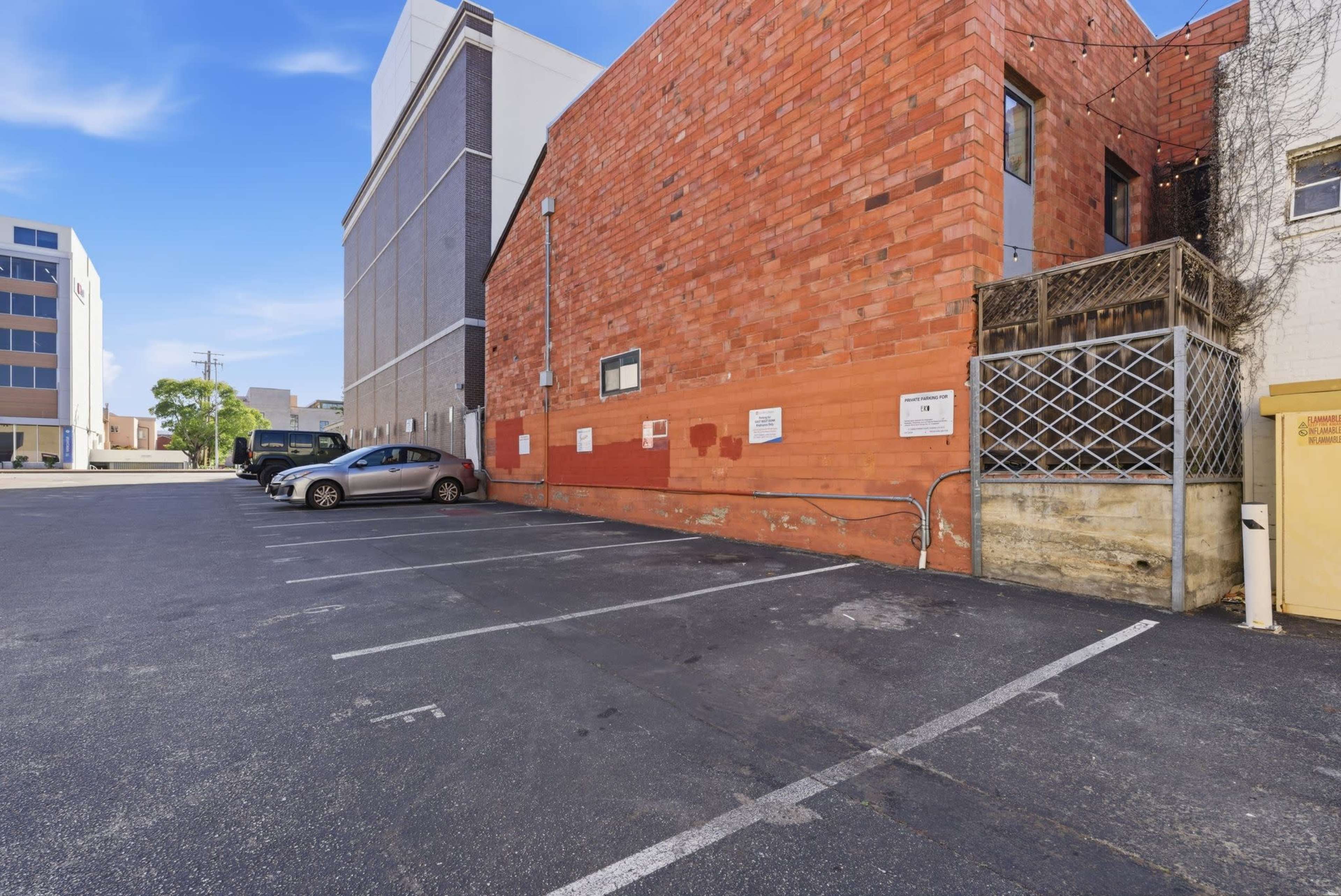 The image shows a parking lot with several vehicles next to a brick building in an urban area.