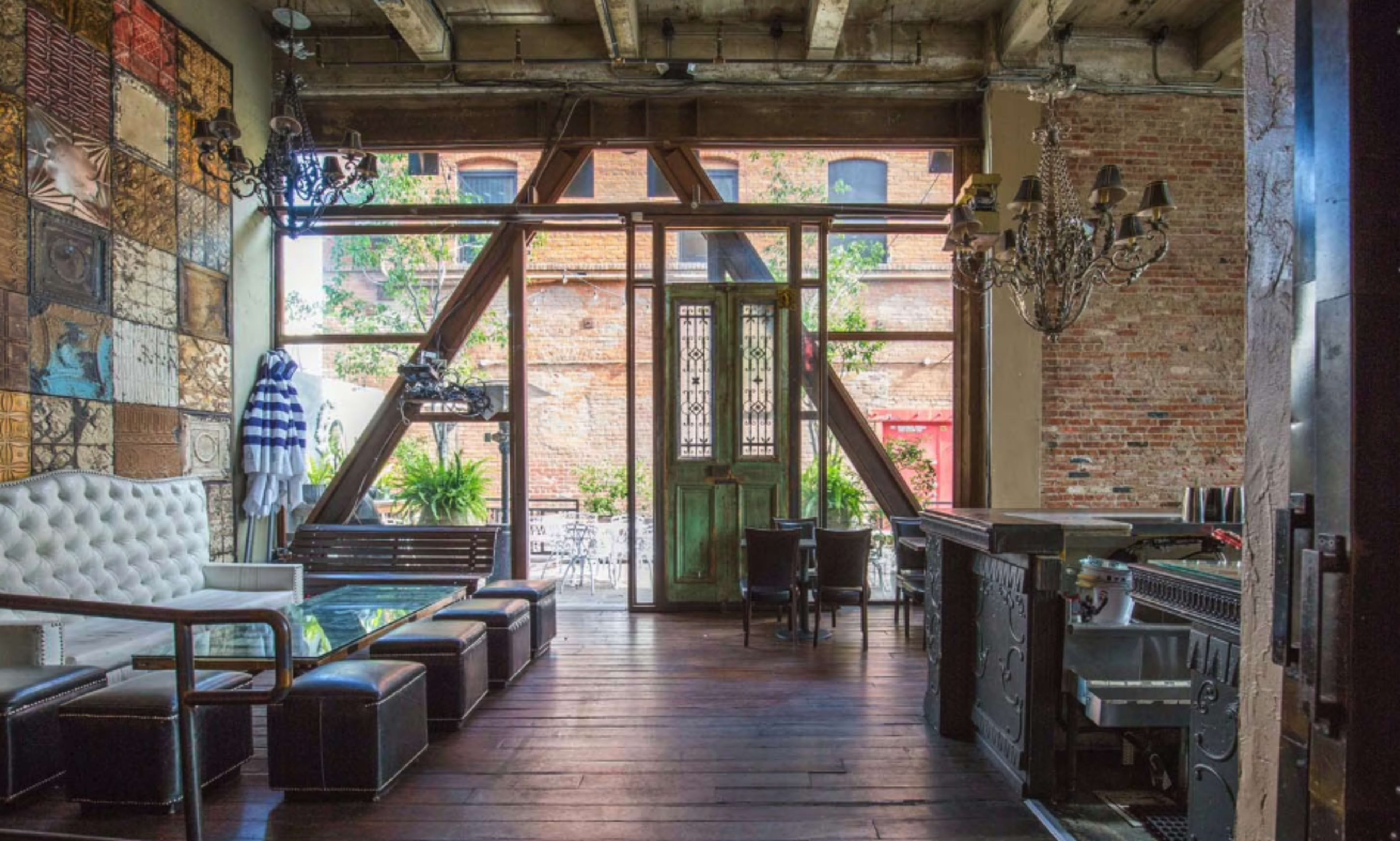 The image shows an industrial-style interior featuring wooden beams, a brick wall, and a mix of modern and vintage furniture in a spacious room.