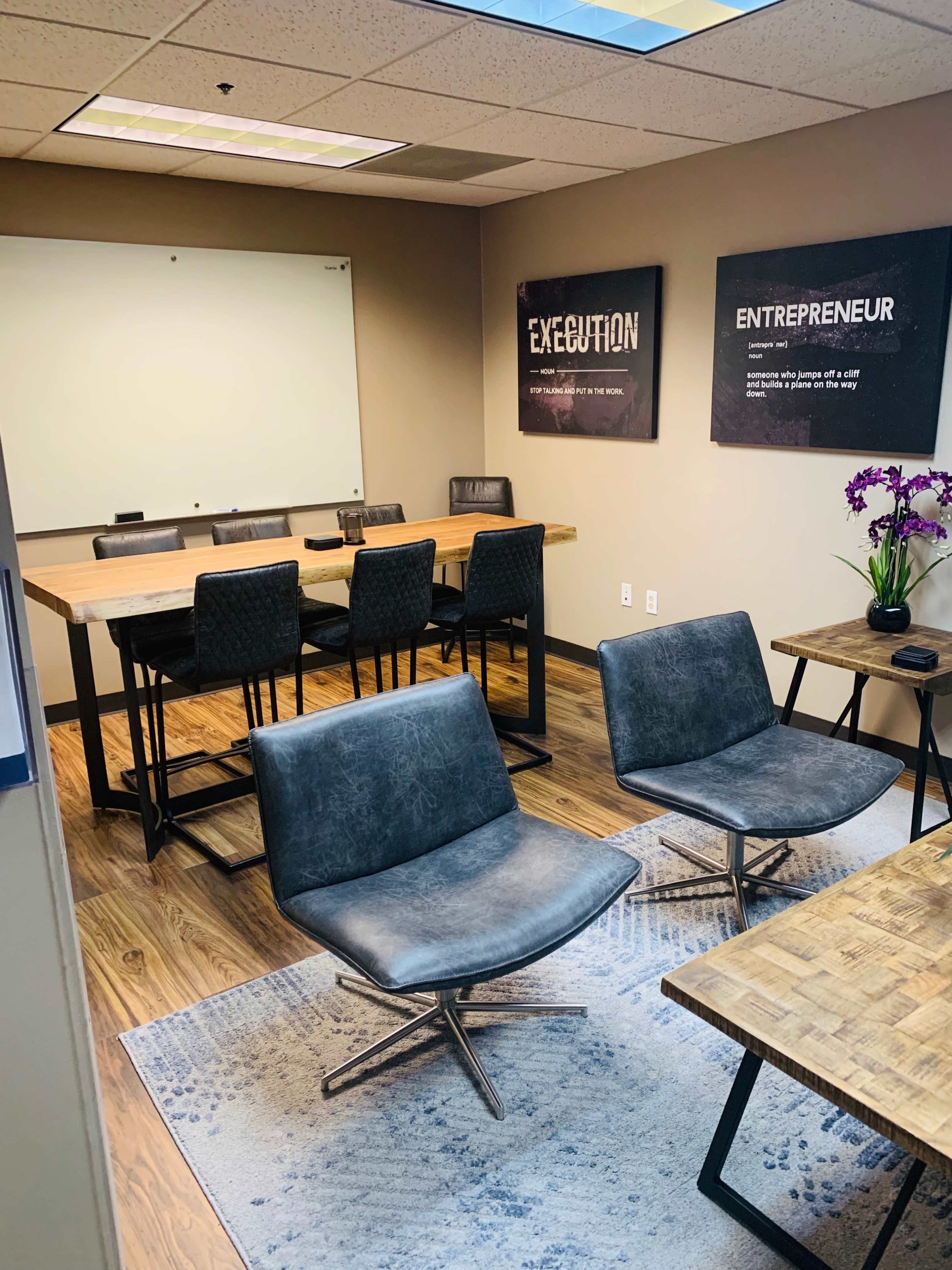 The image shows a modern conference room with a wooden table, black leather chairs, and motivational posters on the walls.