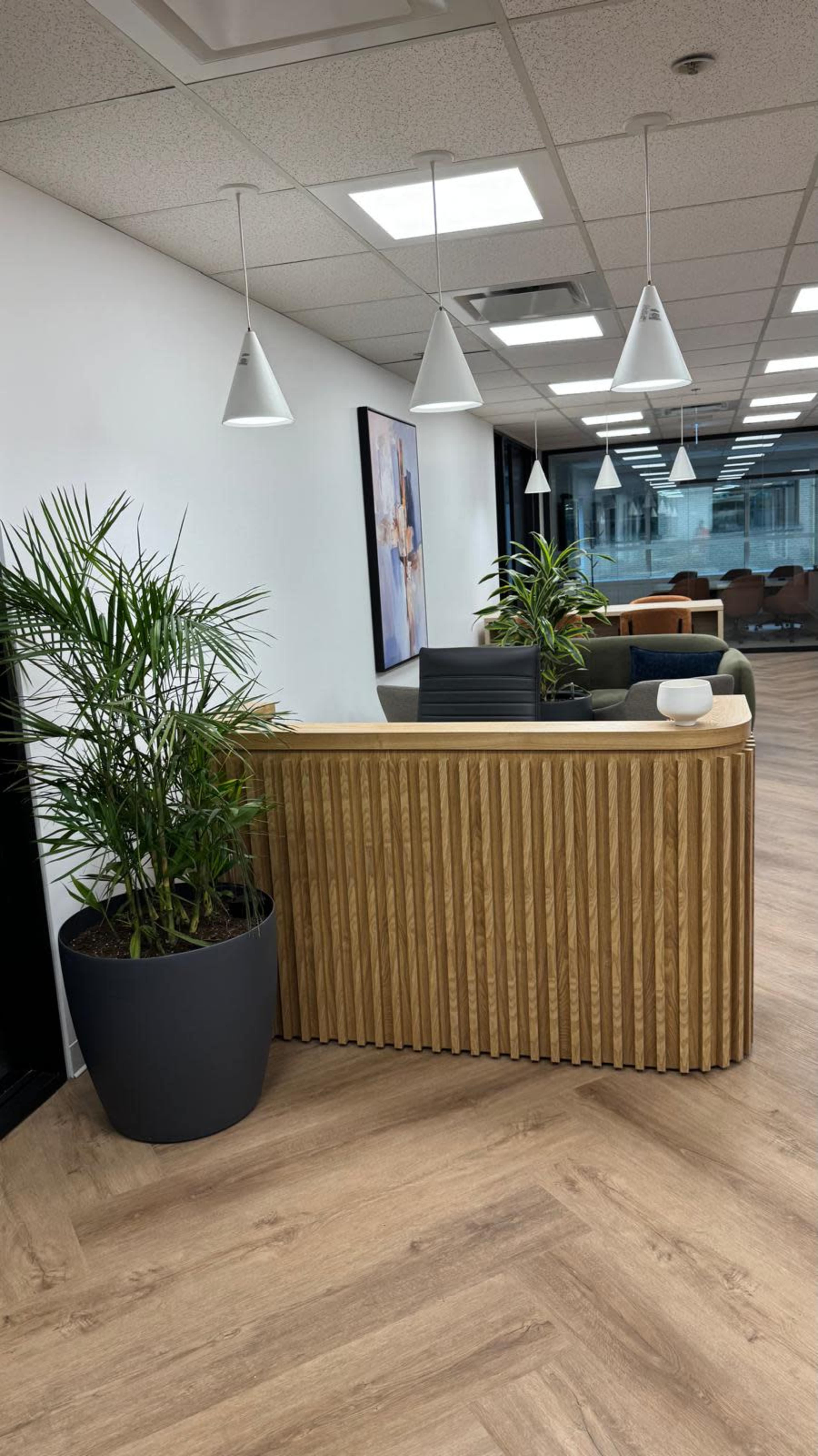 The image shows a modern office reception area with a wooden front desk, potted plants, and stylish pendant lights.