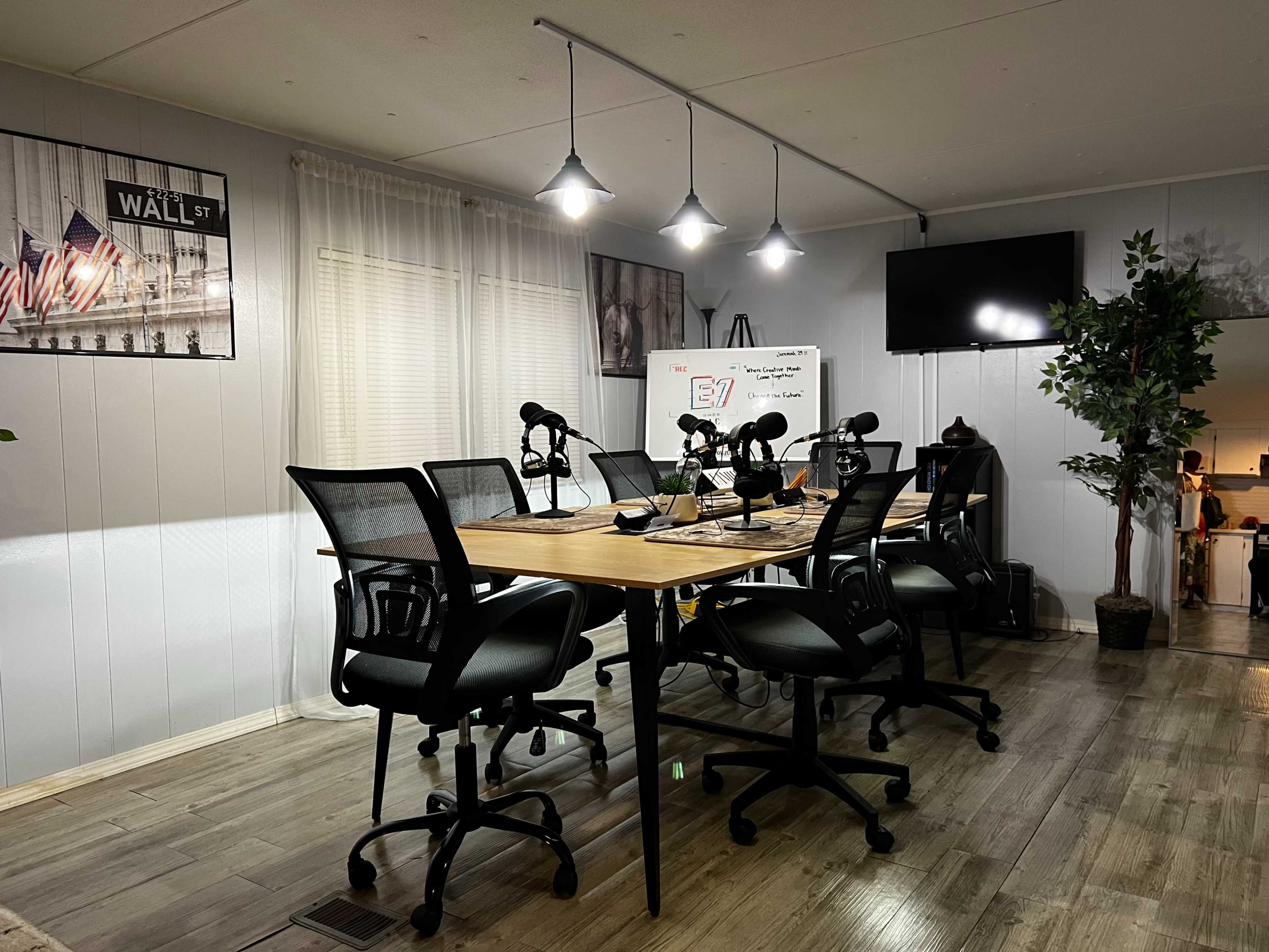 A modern conference room features a long wooden table surrounded by black office chairs, with multiple microphones, a whiteboard, and a wall-mounted television.