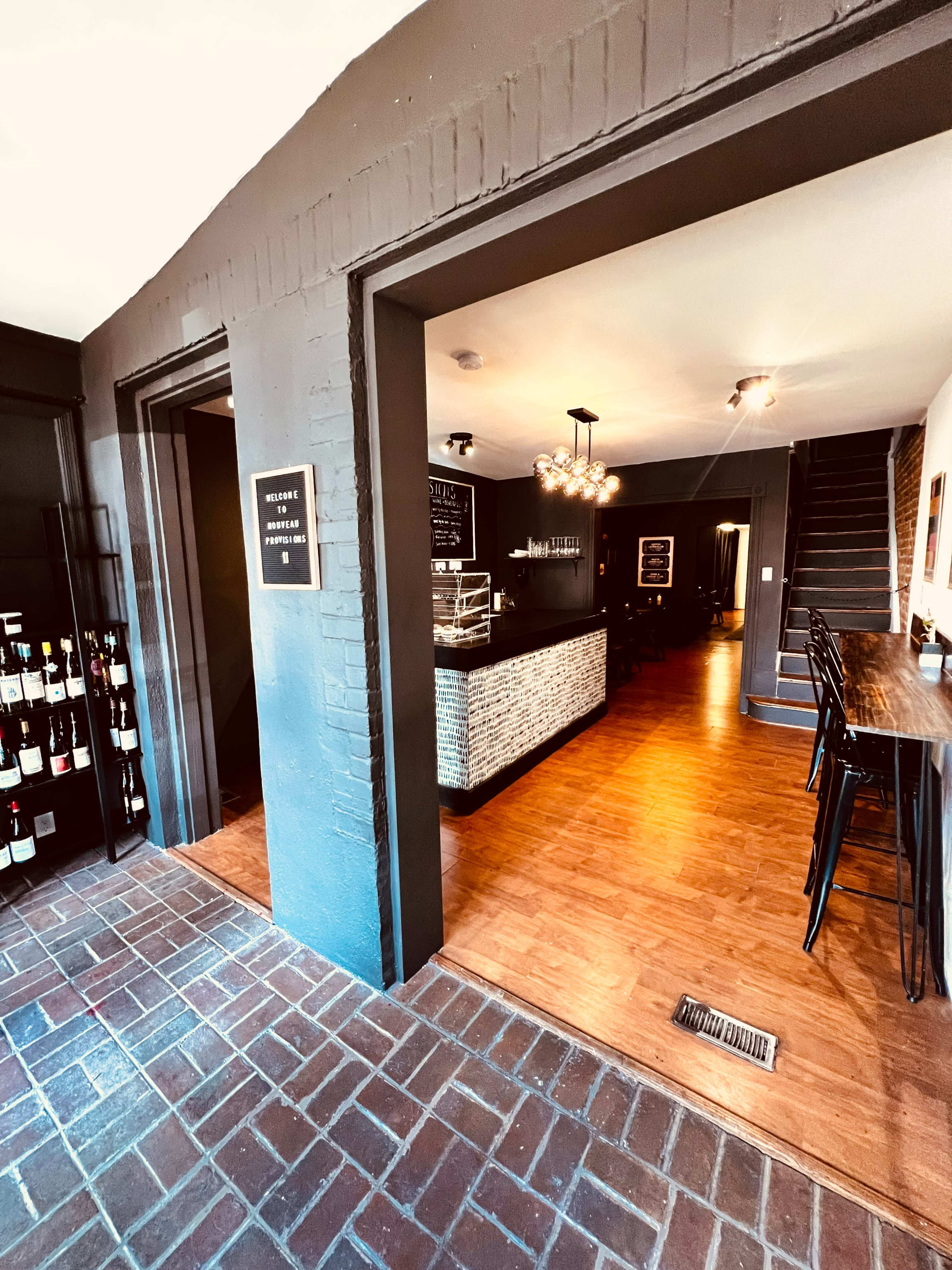The image shows the interior of a restaurant with a counter on the left, wine racks nearby, and a dining area visible in the background.